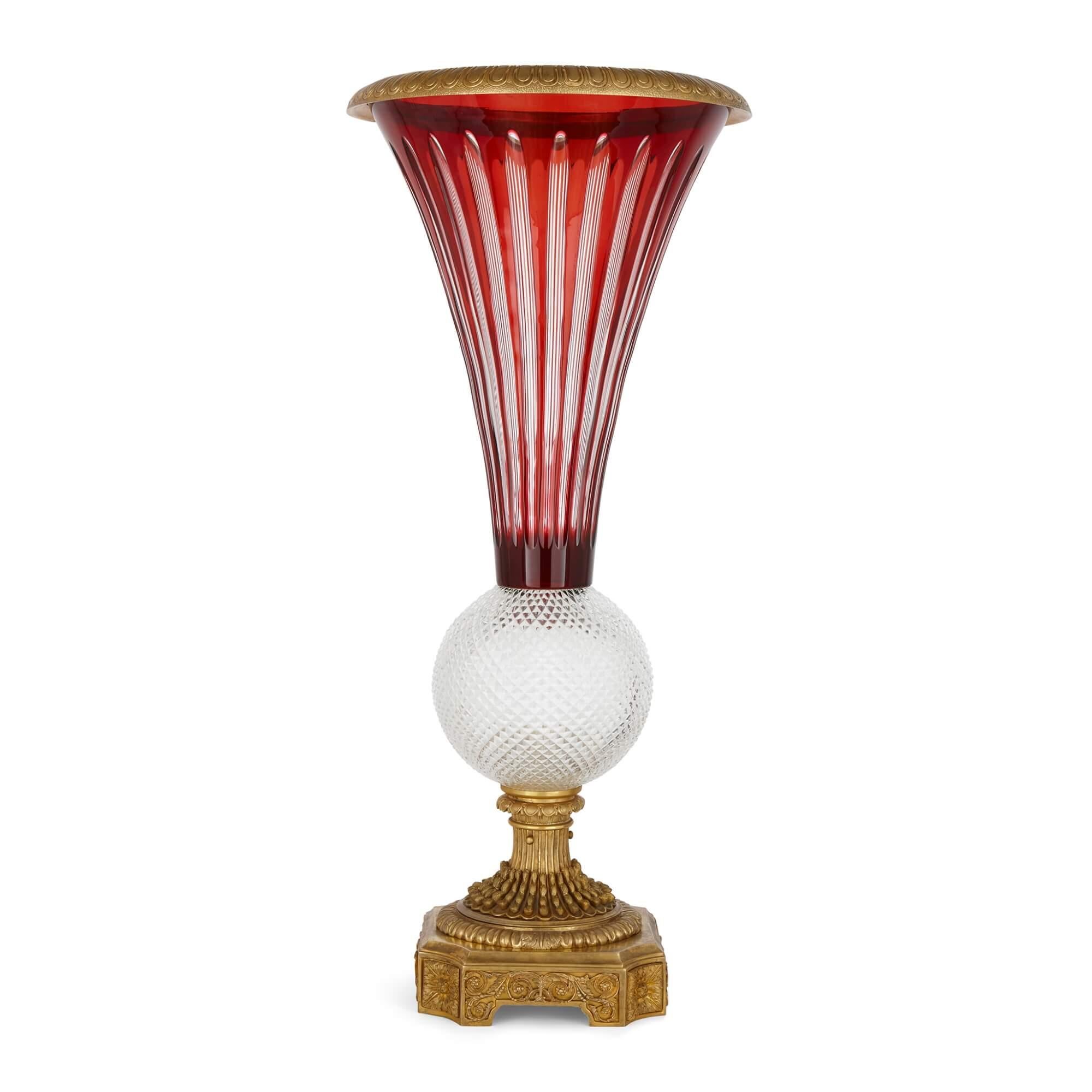 Large gilt bronze, ruby red and clear cut glass vase 
French, 20th century 
Height 80cm, diameter 36cm

The brightly coloured ruby red glass fluted body of the vase, is adorned with delicate clear glass detailing. The vase terminates in a tulip
