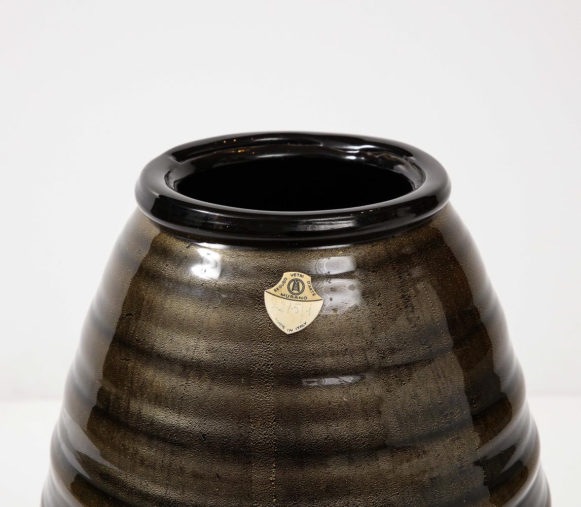 Farbiges Glas, Goldfolie. Großflächige Vasenform aus opakem schwarzem Glas mit horizontalen Rippen und Goldeinschlüssen. Aufgetragene Lippe und Basis.