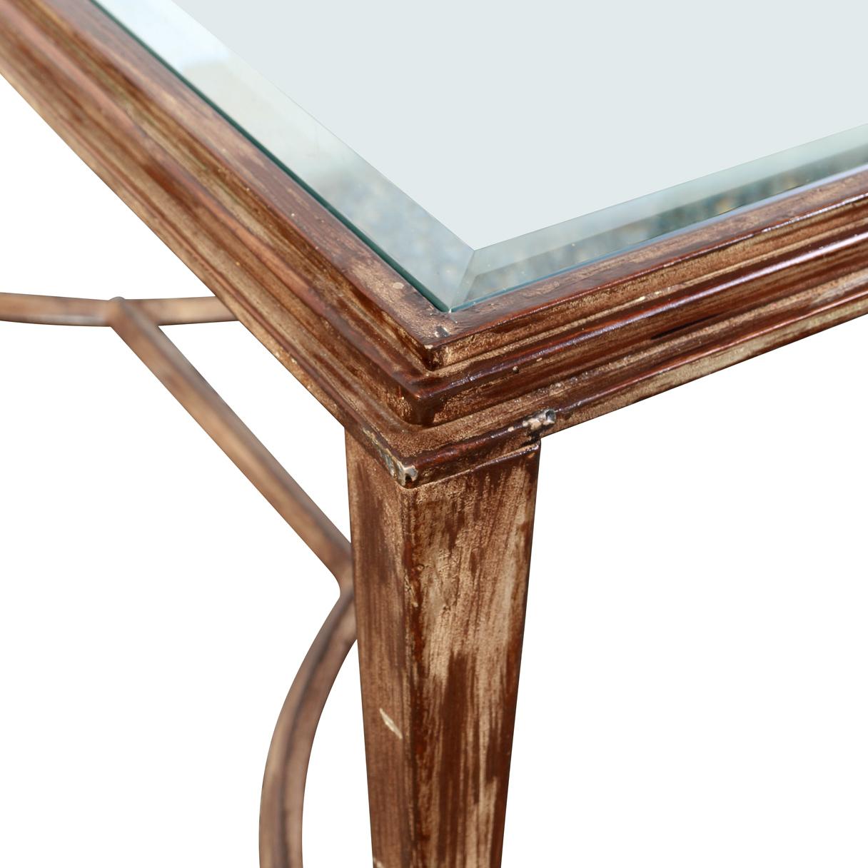 A large coffee table that features a gilt metal frame and a beveled glass top. The base is designed with a curved X-form silhouette, lending the piece a sense of movement and architectural flair. The beveled glass top offes a clear, polished surface