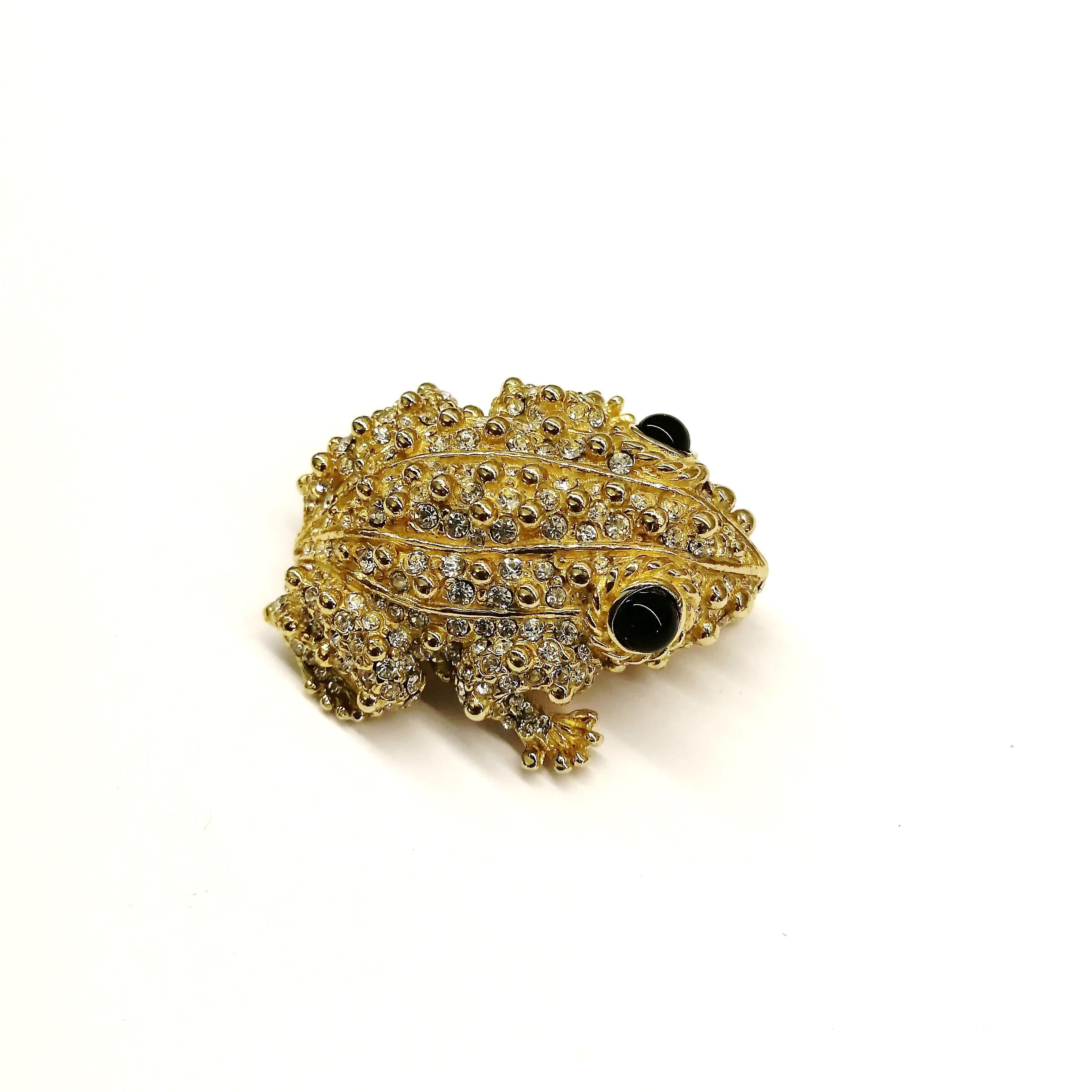 A charming gilt metal and clear paste 'frog' or 'toad' brooch, made by Ciner, the quality as expected from this well known designer. The surface has gilt 'bobbles' interspersed amongst the clear pastes, giving a shimmering and textured surface.
Sits