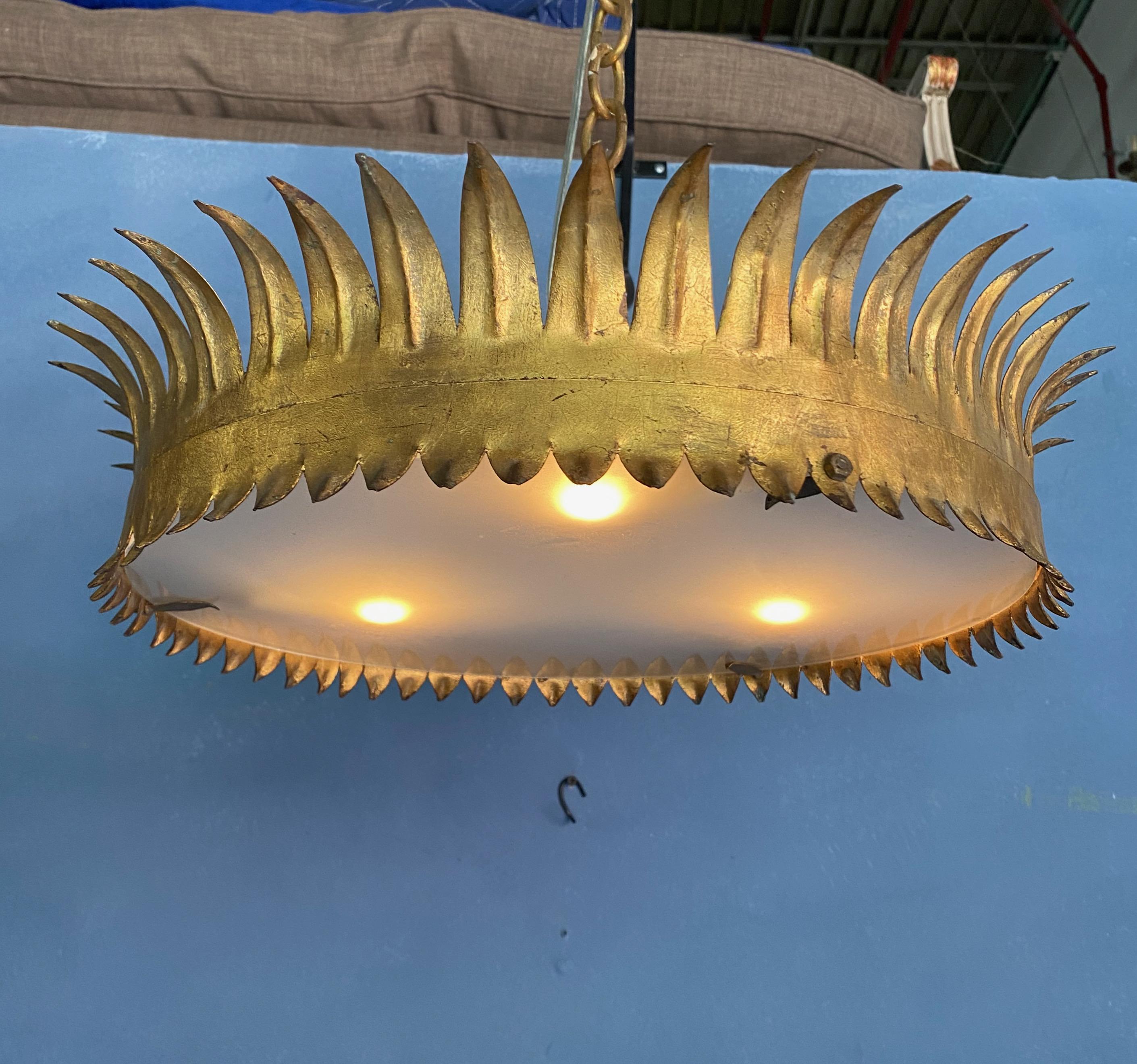 A large scaled crown ceiling fixture composed of pointed rays on the upper part and smaller ones on the lower part. The metal has a rich hand gilt  finish. The acid etched glass diffuser is held in place by 3 clips that makes change the light bulbs