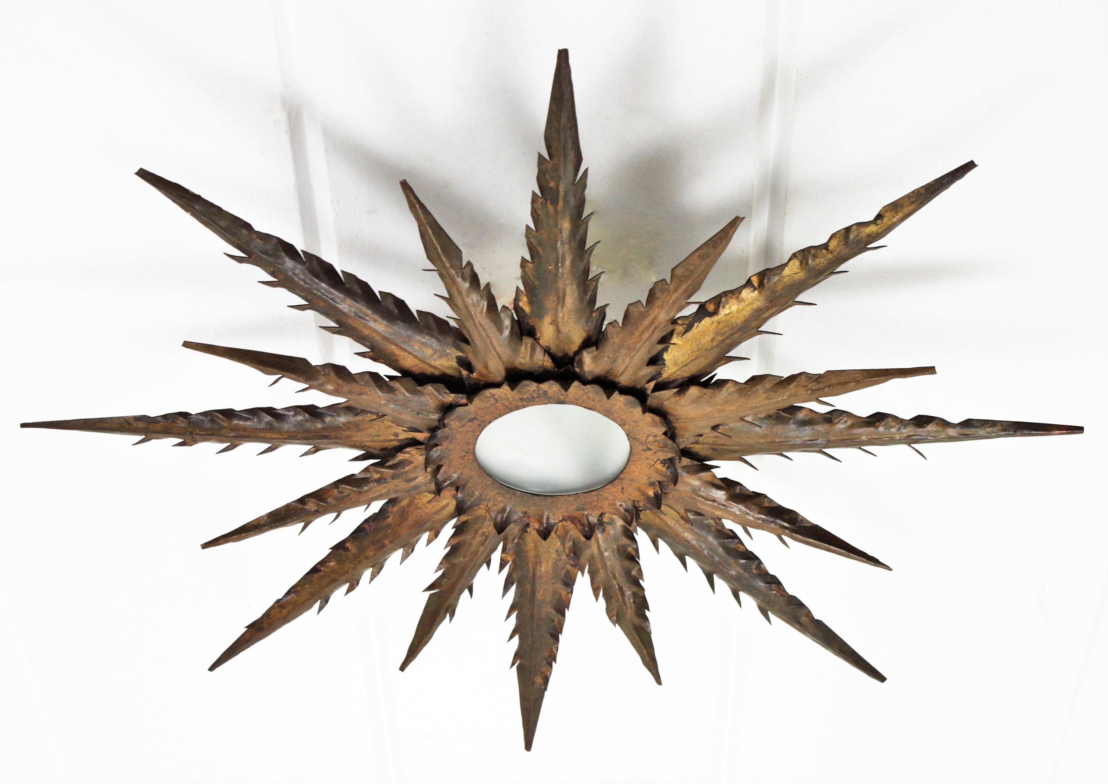 Rare handcrafted parcel-gilt iron sunburst / starburst shaped flush mount with frosted glass, Spain, 1940s-1950s.
This Brutalist flush mount has two layers of rays in different sizes with jagged pointed edges. It has a terrific aged patina with