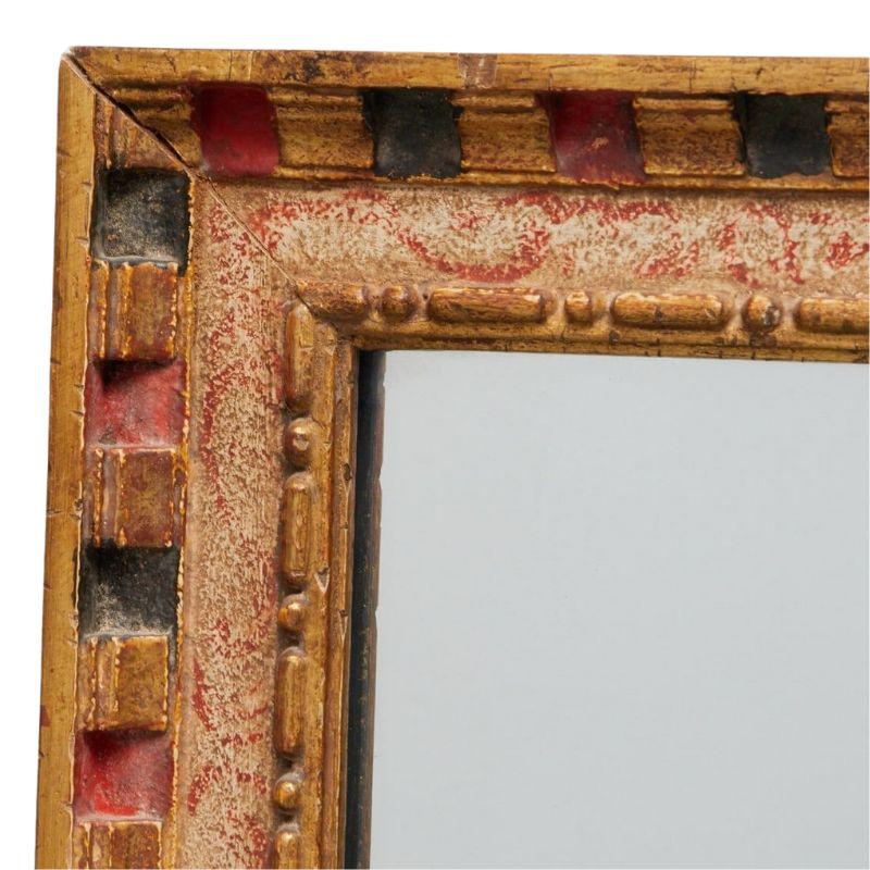 Ce grand miroir polychrome en bois doré présente un cadre sophistiqué à moulures en denticules, orné d'un mélange captivant de dorures, de rouge et de noir. La forme rectangulaire du miroir offre un design classique et polyvalent, parfait pour