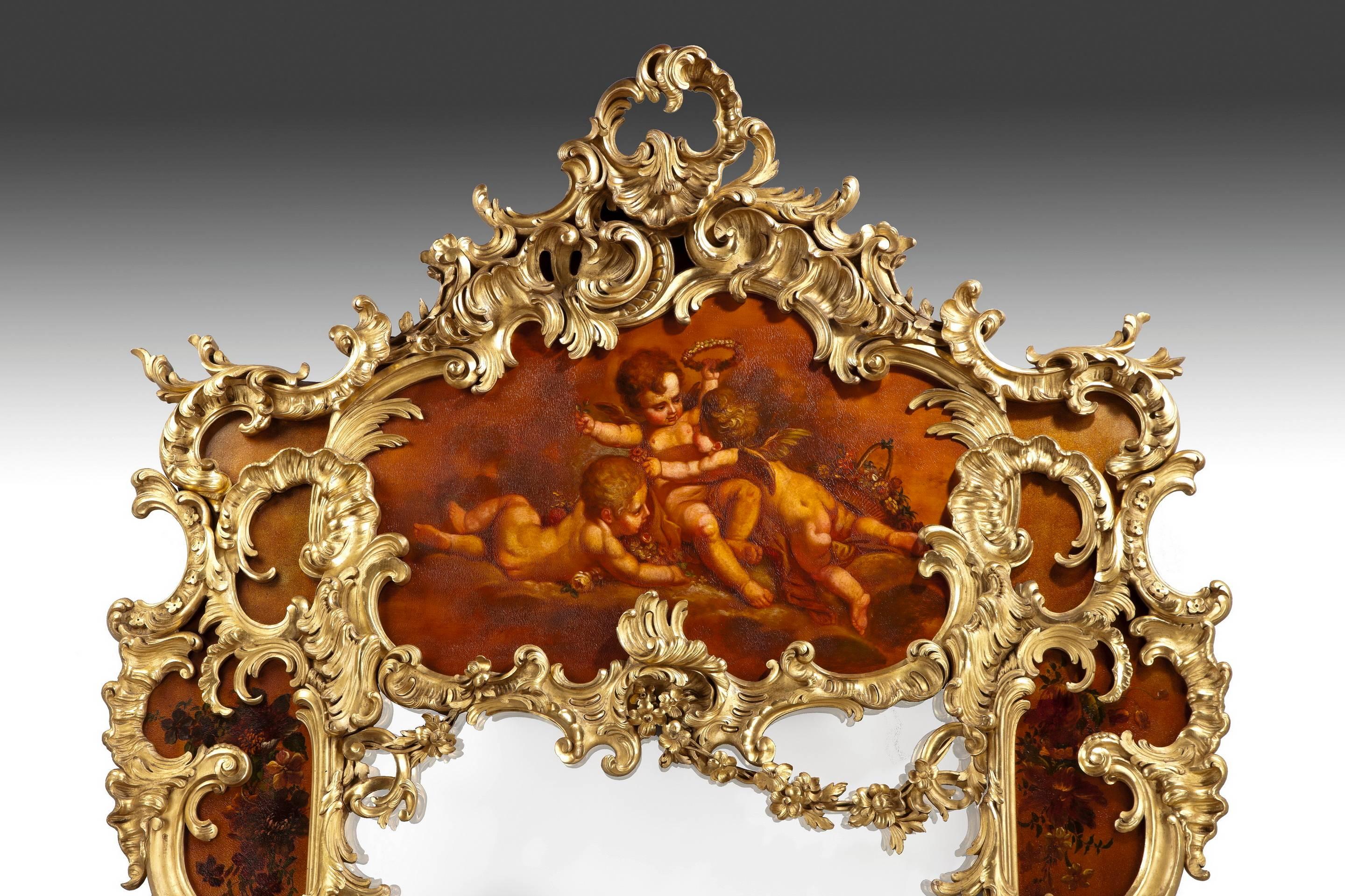 This grand mirror has a central rectangular plate framed by ‘vernis Martin’ panels of floral sprays centered on a charming scene of three putti in a bower, one being crowned with a floral circlet. These are overlaid with exuberant giltwood garlands,