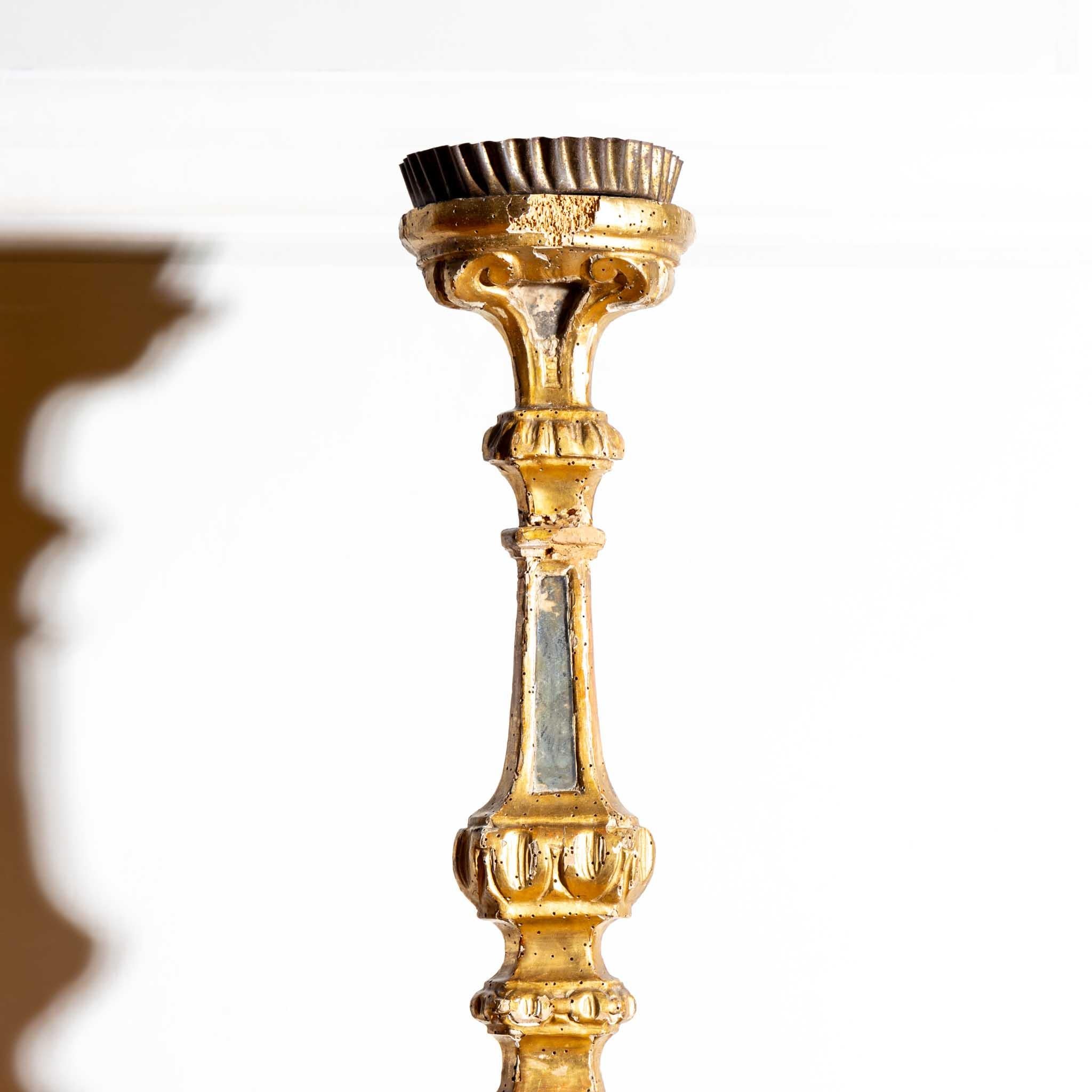 Baroque altar candlestick with a three-legged stand and a balustered shaft with a gold-patinated and dark accentuated setting and a wavy brass spout. The frame is bumped in places, traces of former woodworm infestation.