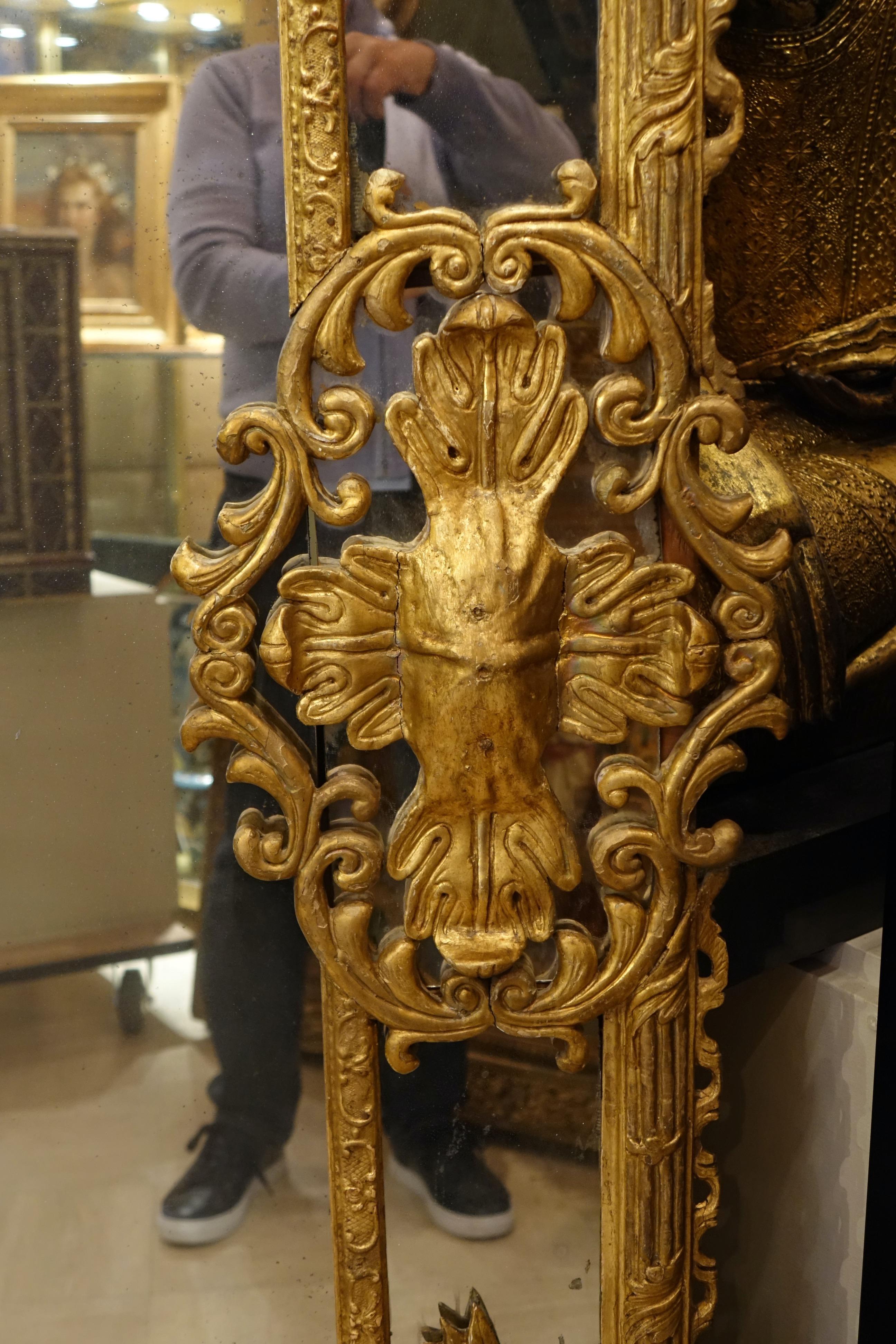 Grand miroir en bois sculpté et doré, décoré de rinceaux, de feuilles d'acanthe, de colonnes cannelées et de deux grands motifs en forme de croix sur chaque face. L'ensemble repose sur des pieds griffus. Verre de mercure et pare-closes. Parquet à
