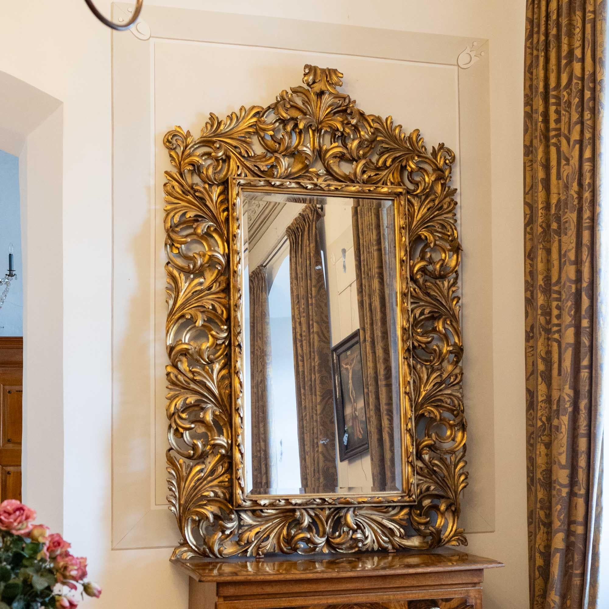 Grand miroir mural Florentine avec ancienne glace partiellement aveugle. Le miroir mural est entouré d'un grand cadre en bois doré en forme de vrilles ajourées ou d'ornements de feuilles.