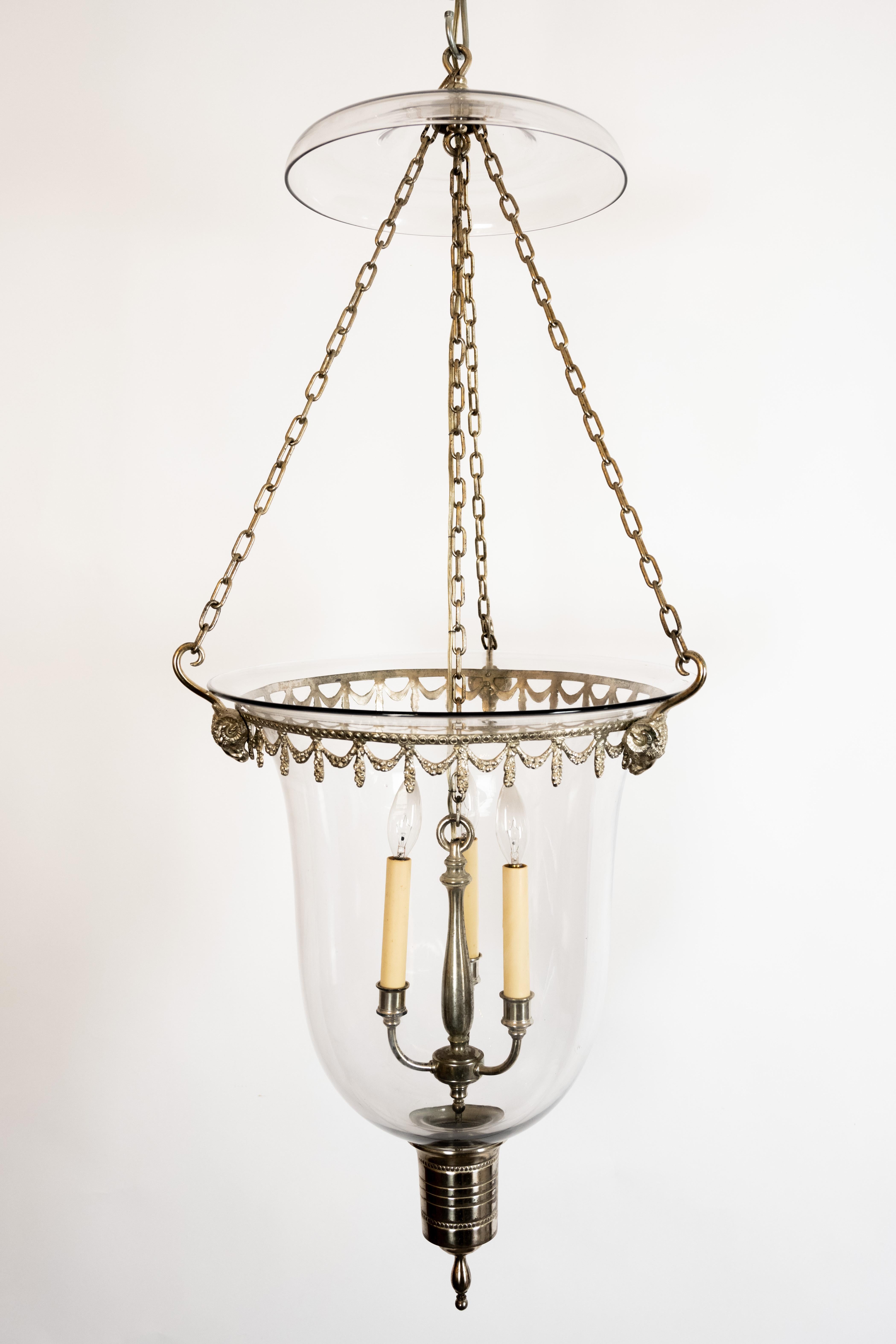 Georgian style hanging glass lantern. Silver chains suspend an ornate wreath frame featuring Rams head details from the glass smoke bell. Three Candelabra bulbs attached to a baluster shaped column provide illumination. The bottom of the blown glass
