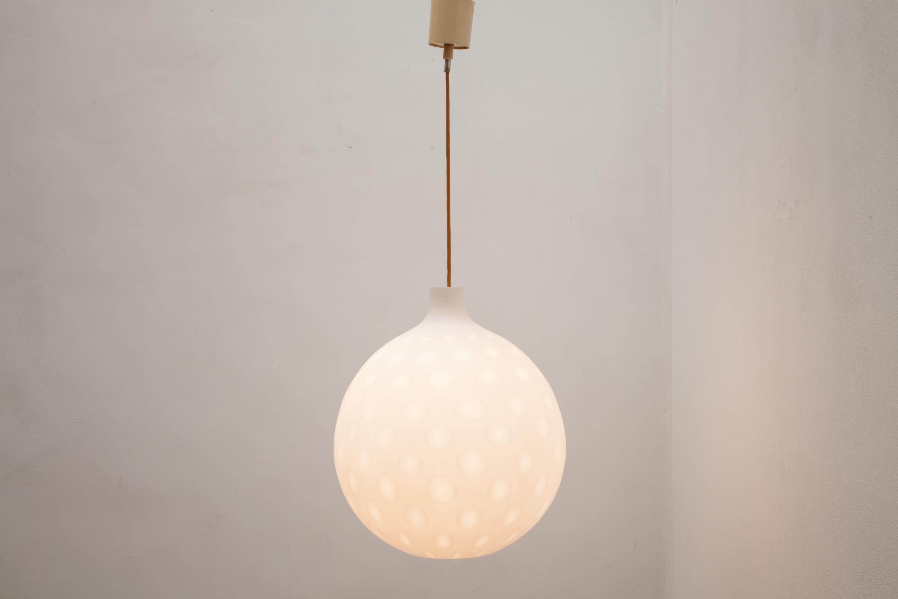 Midcentury glass globe pendant by Aloys Gangkofner for Peil & Putzler, 1958.
This model globe pendant features an organically shaped thick milk-white glass shade with a moon-like circular pattern in the glass. 

The fully functional piece is