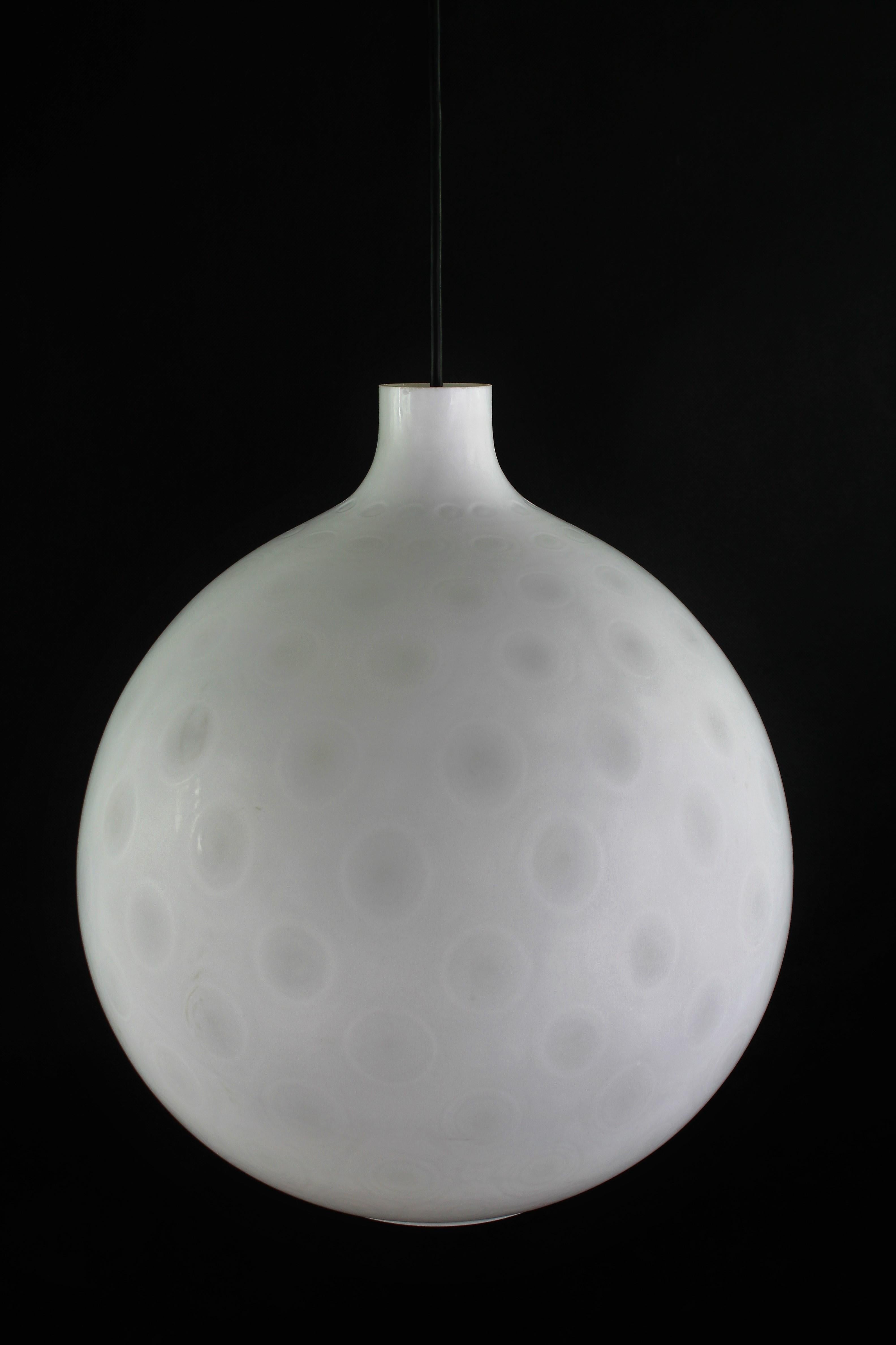 This rare large lamp is a true design classic from the 50s/60s. This lamp in an unusual design has an organically shaped shade made of thick, milk-white glass with a moonlike, round pattern in the glass.
This vintage lamp is an original and gives a