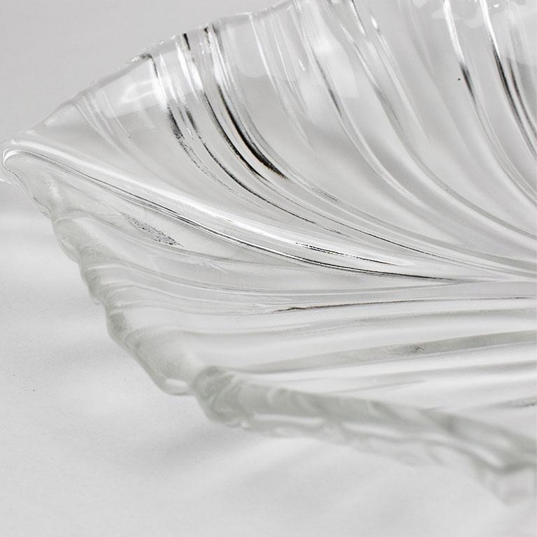 Una gran fuente de cristal con forma de hoja de palmera y una flor de hibisco en el tallo. La parte superior de la fuente es lisa, y la inferior está tallada para mostrar el veteado de las hojas y el hibisco. Esta fuente sería una gran adición a tu