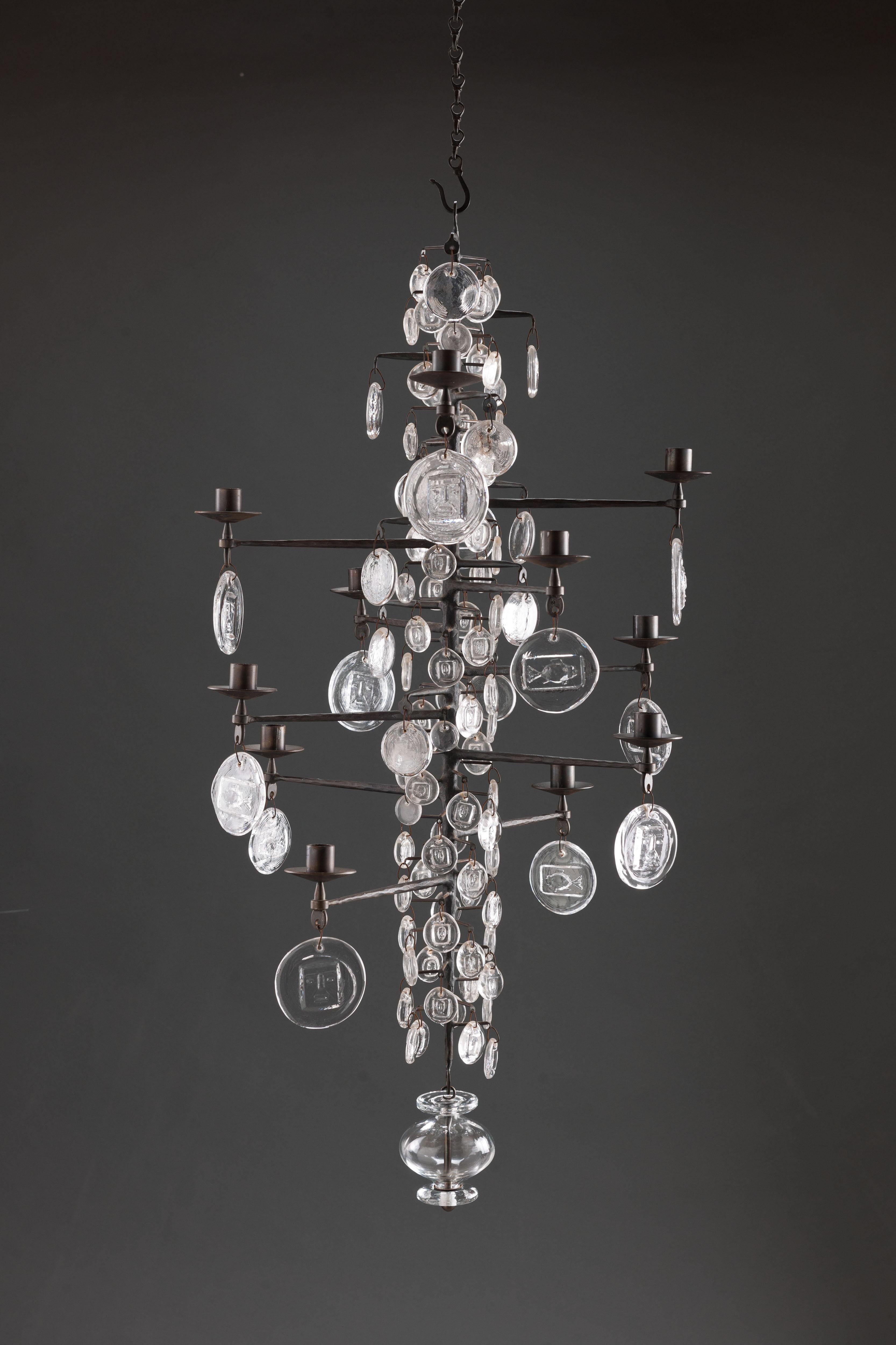 Cast iron, mouth blown and pressed glass 12-arm chandelier for 12 candles by Swedish designer Erik Hoglund with images of animals and faces. 
Boda glassworks, Axel Stromberg ironworks, Sweden, 1957. 

Early edition on welded chain. Rarely offered