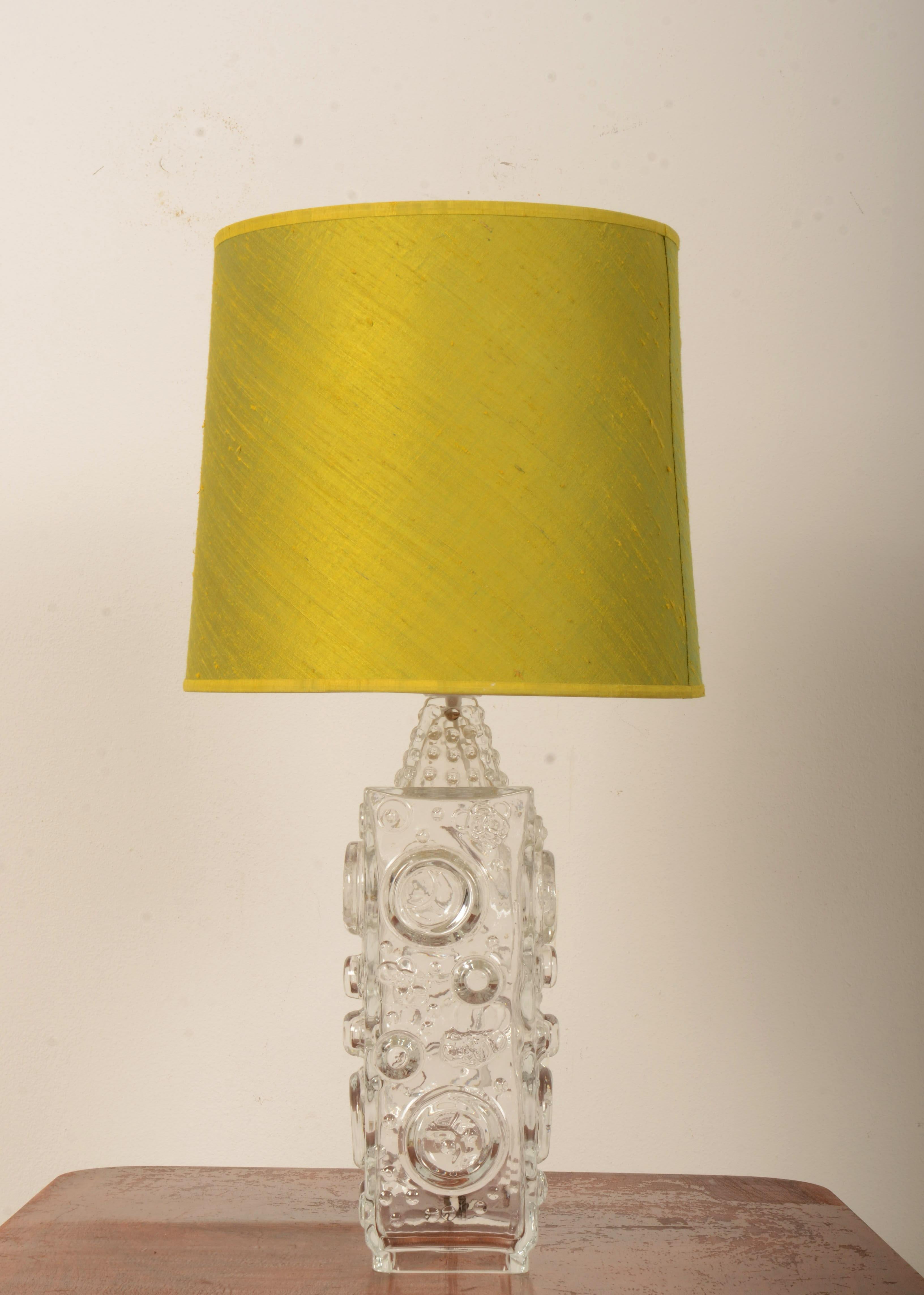 Grande base carrée en verre moulé décorée de cercles et de fossettes en bas-relief, équipée d'une prise E27 et d'un abat-jour en soie verte. Conçue par Josef Schott dans les années 1960 pour Smalandshyttan, au Danemark. 
