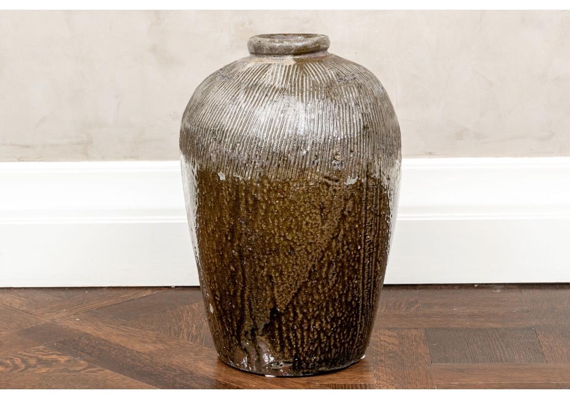 A large organic form thick-walled ceramic jar in brown glaze with a rolled neck, ribbed shoulder and speckled body. 
Measures: Height 19.5” diameter 13”. 
Condition: overall good with some expected and acceptable chips, presenting very well.
