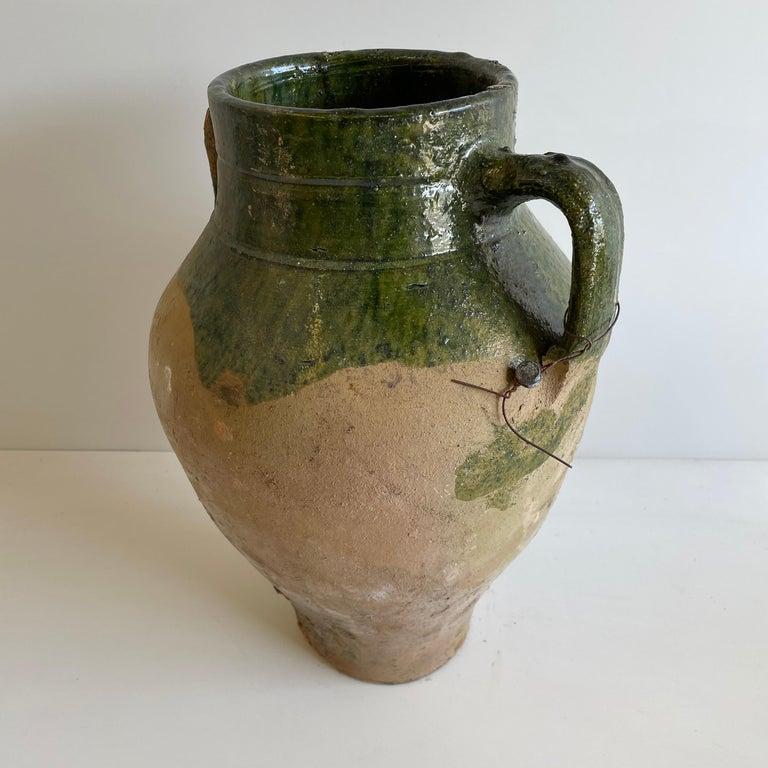 Large clay pot with handles dipped in a dark olive green glaze.
Imported.
Measures: 15” H x 12” W x 11” D.
