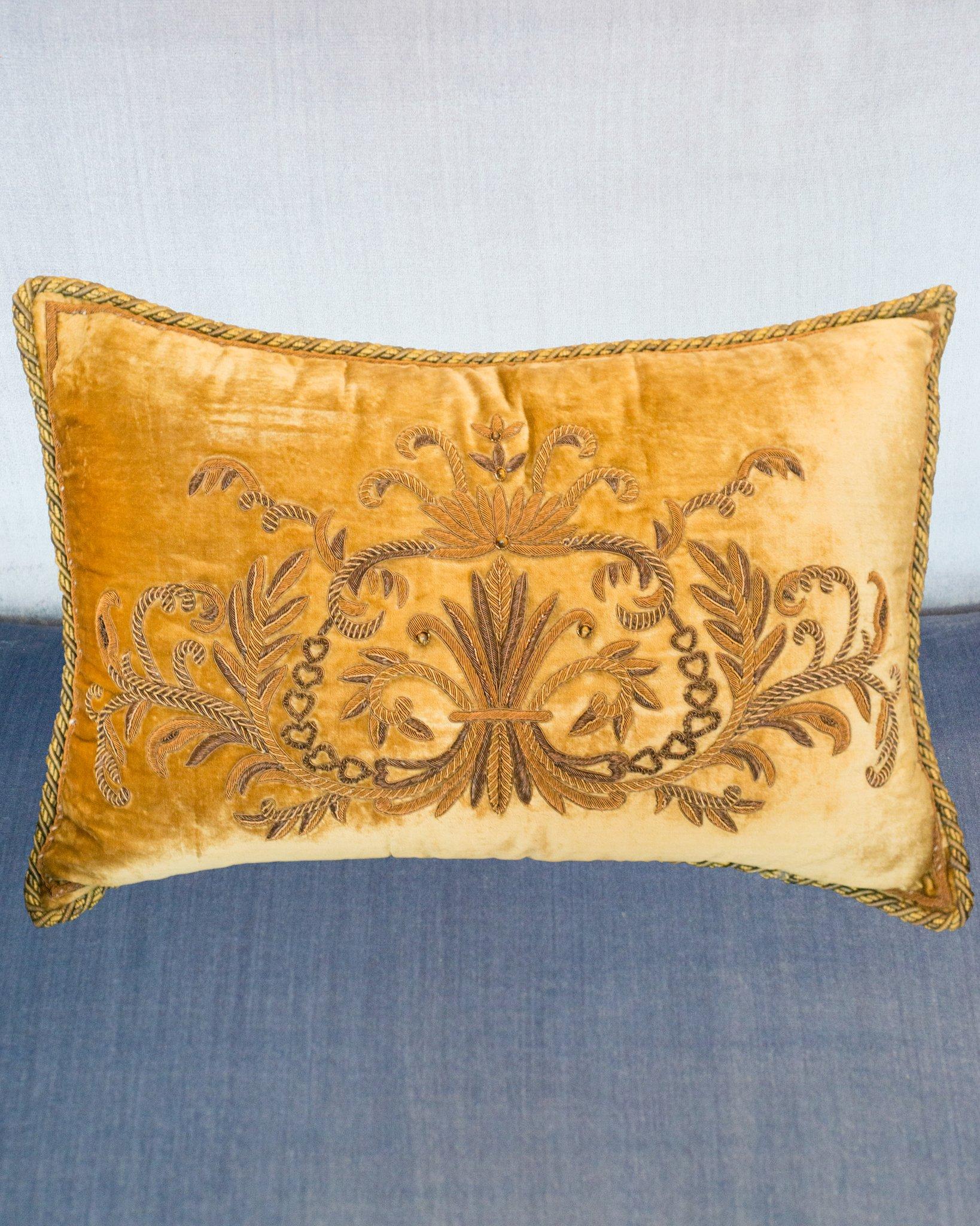 A large gold velvet pillow with ornate metallic applique, tigers' eye beads, and a metallic rope trim. Button and loop closure on reverse, entirely filled with down and feather.