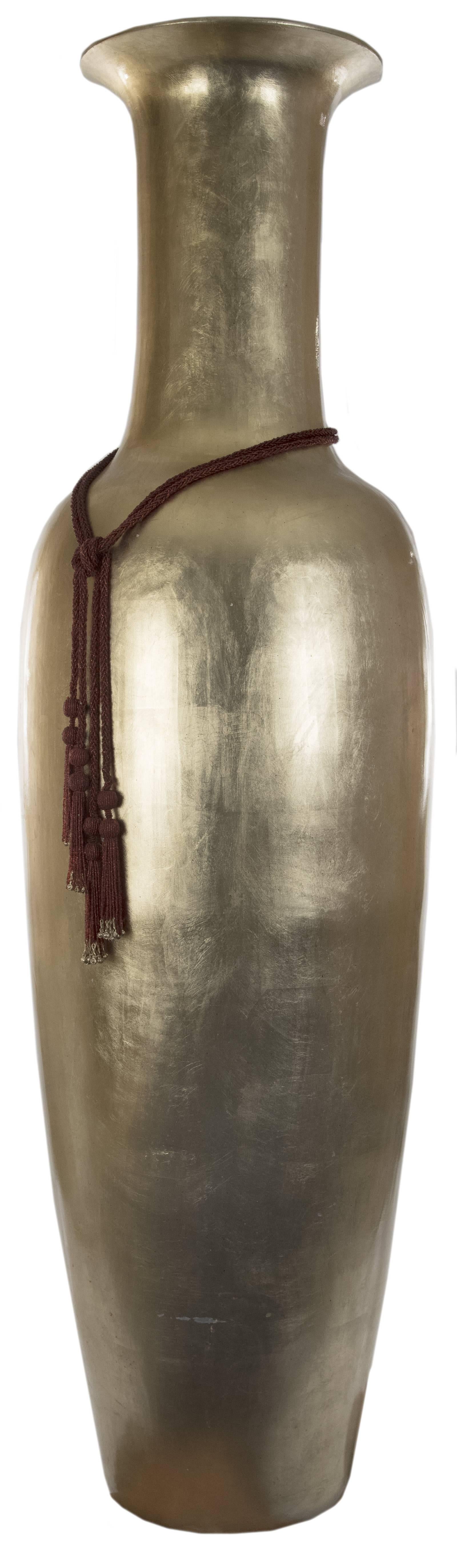 A large floor vase with a wide and flared rim above a narrow cylindrical neck leading to an elongated baluster body on a flat base, the entire surface covered with gold leaf. Measures: 71 x 21 inches.