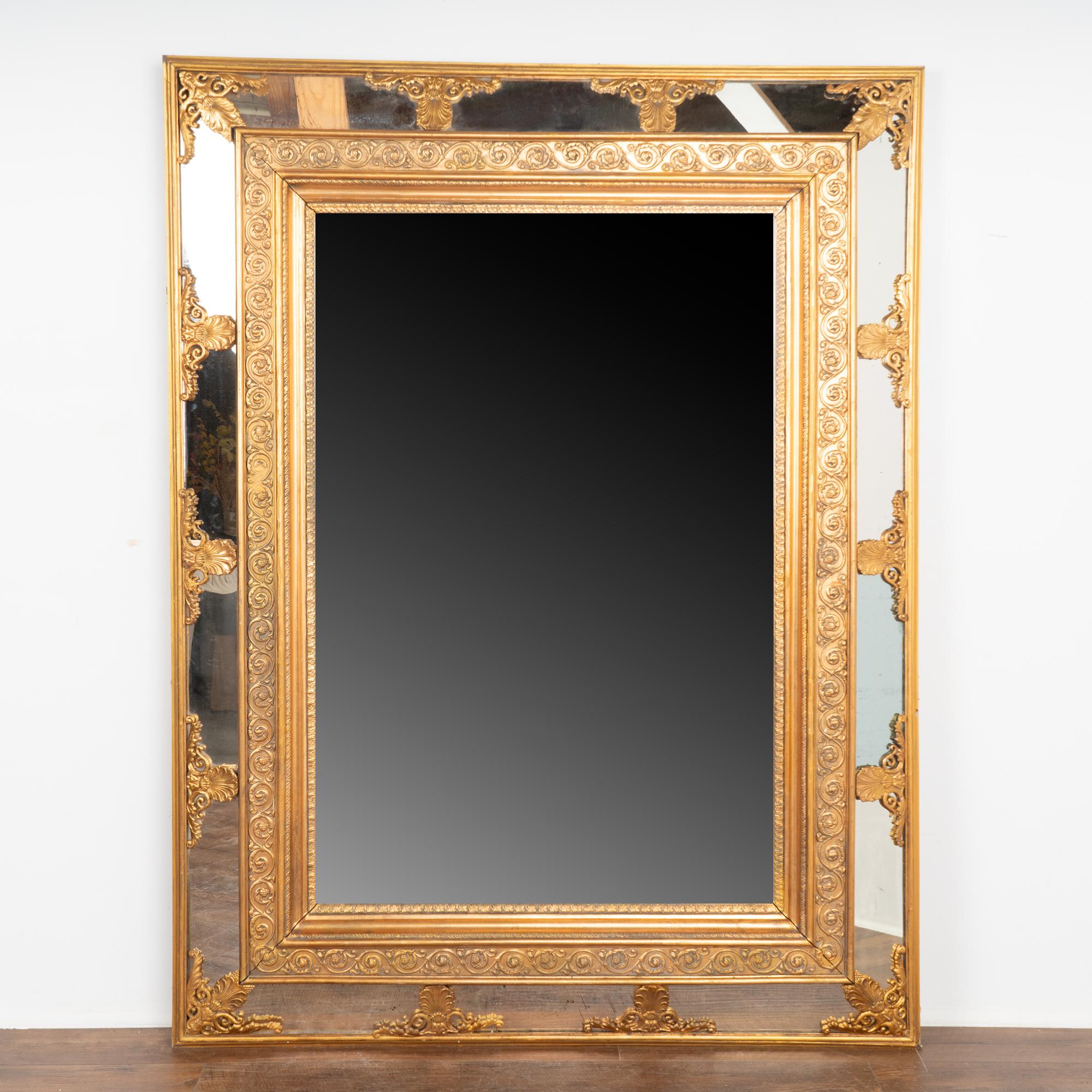 This impressive large 6' gold gilt mirror has scallop flourishes accenting the canted mirrored sides. 
There is expected age-related wear as seen where the gilt has been worn off, wood is nicked or cracked (including old repairs), aged separation at