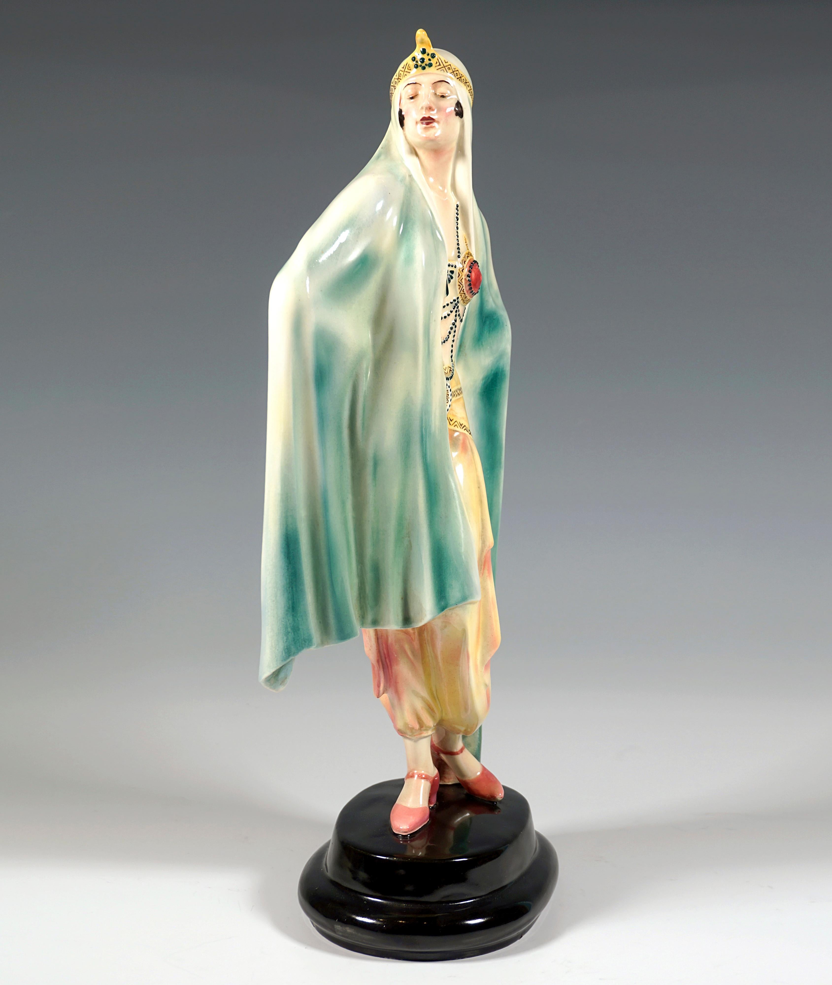 Sehr außergewöhnliche dekorierte Goldscheider Art Deco Keramikfigur aus den 1920er Jahren:
Darstellung einer stehenden Dame in orientalischem Gewand, die stolz zur Seite blickt, eingehüllt in ein großes blaugrünes, bis zum Boden reichendes Tuch, das
