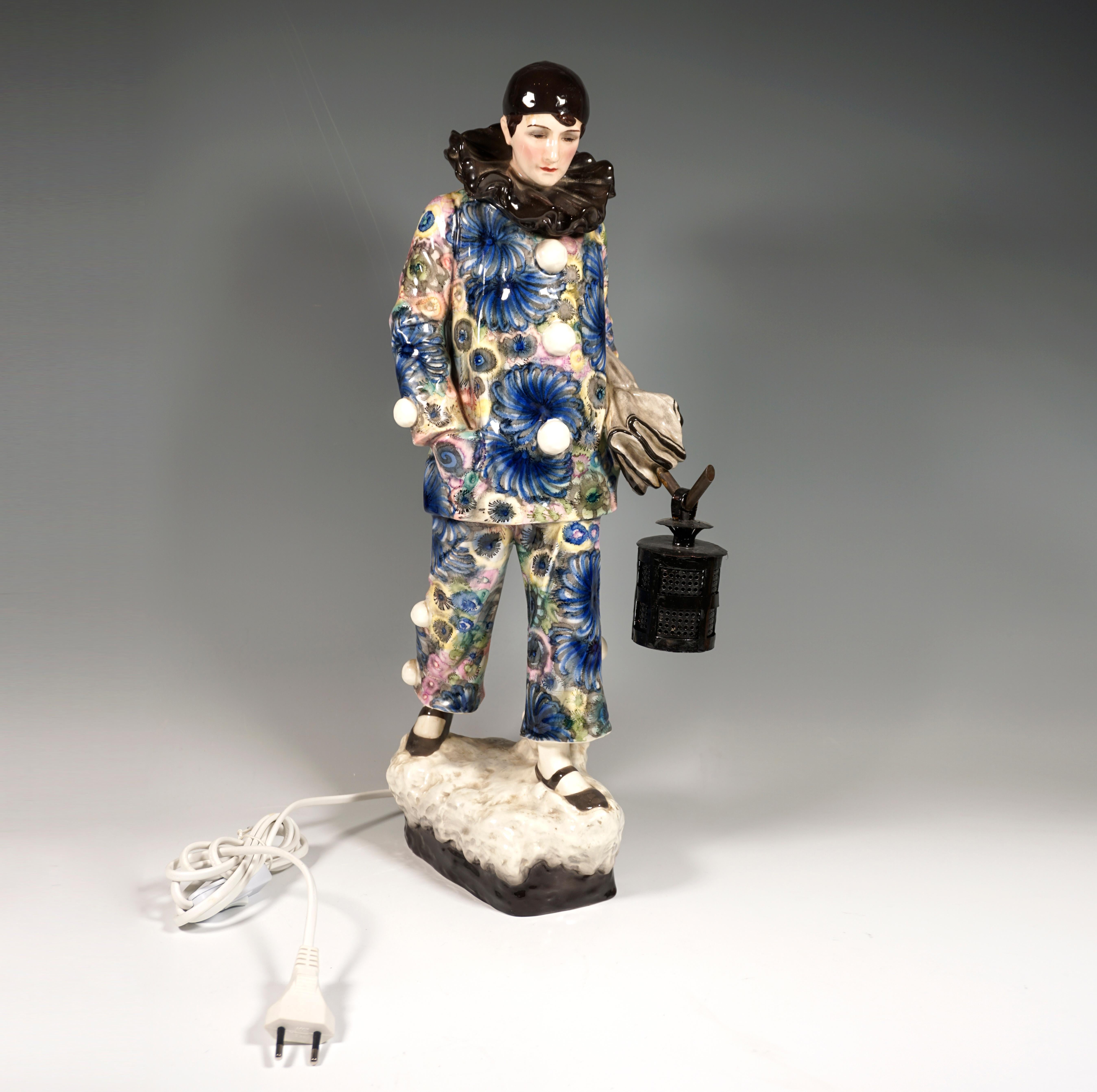 Exceptional goldscheider figurine with lamp of the 1920s:
A harlequin lost in thought is depicted in a costume elaborately decorated with a fine floral pattern in shades of blue and yellow. His cap, the ruff and the strap shoes are kept in dark