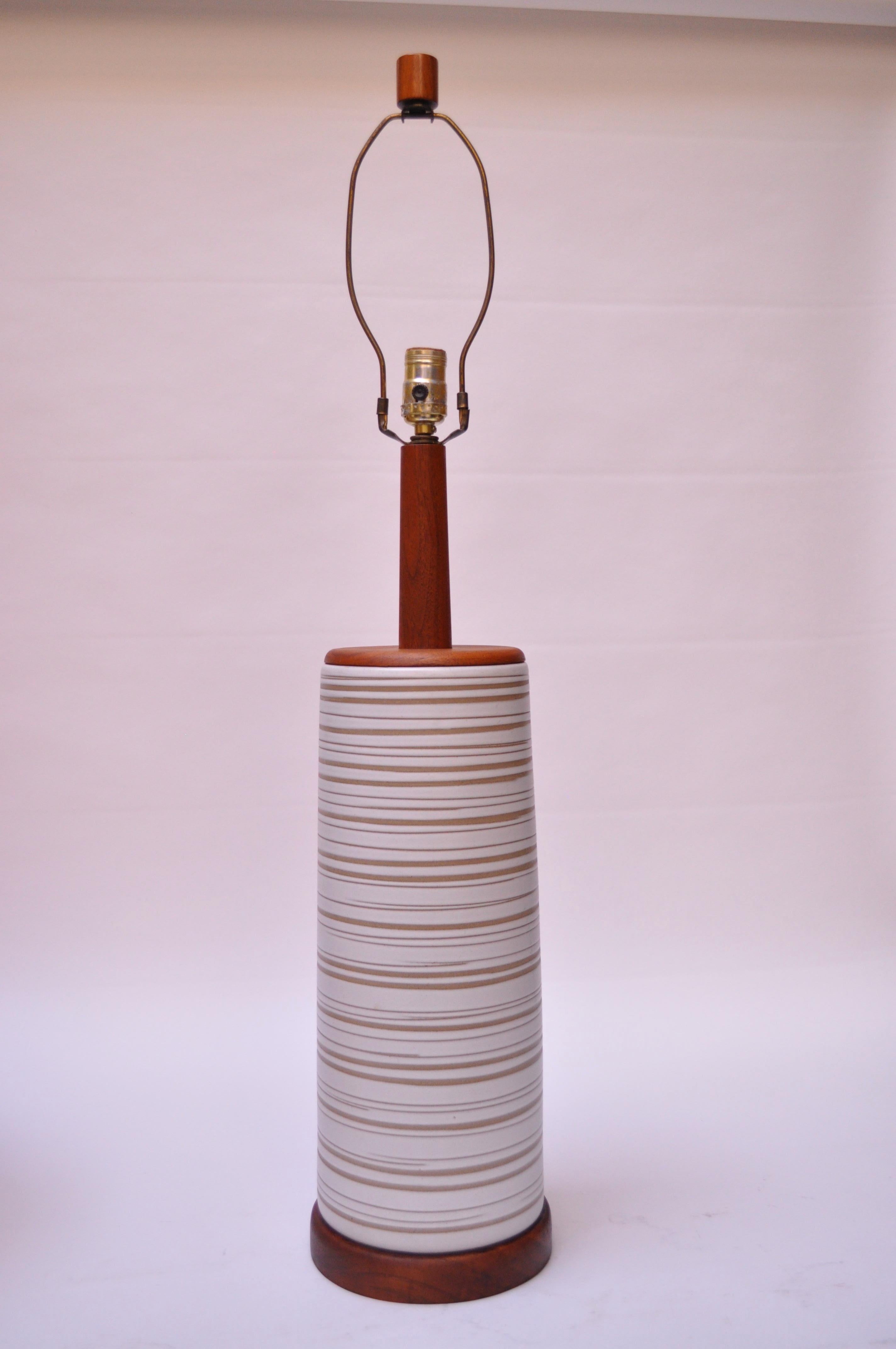 This large Martz for Marshall Studios table lamp features a pale grey body with banded sgraffito decoration, exposing the unglazed surface beneath. This example showcases the rich walnut, present in base, stem / surface, and finial.
Excellent,