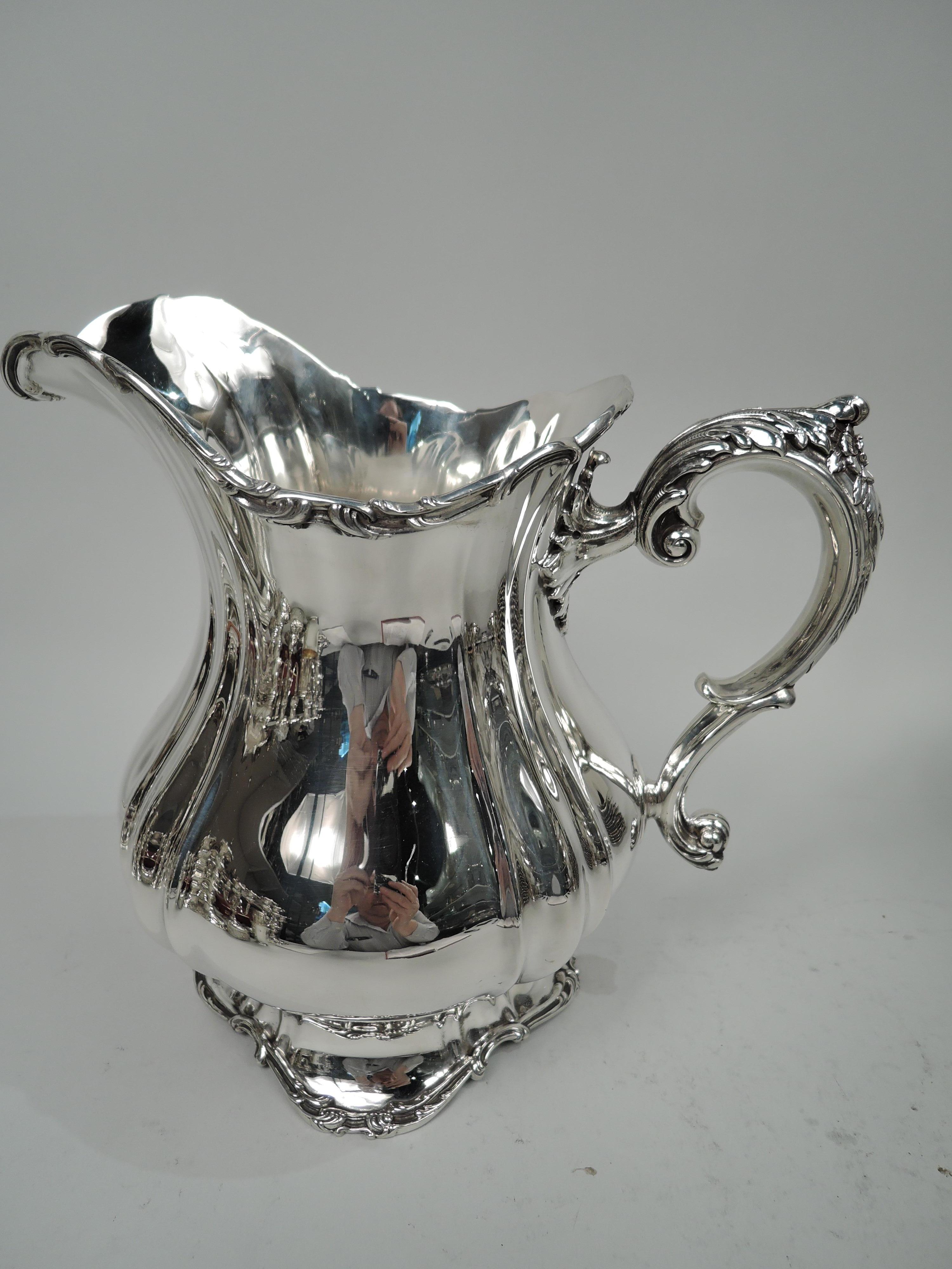 Edwardian Classical sterling silver water pitcher. Made by Gorham in Providence in 1904. Fluted baluster with helmet mouth and leaf-mounted and leaf and flower-capped s-scroll handle; raised and wavy foot. Rims have applied scrolls. Fully marked