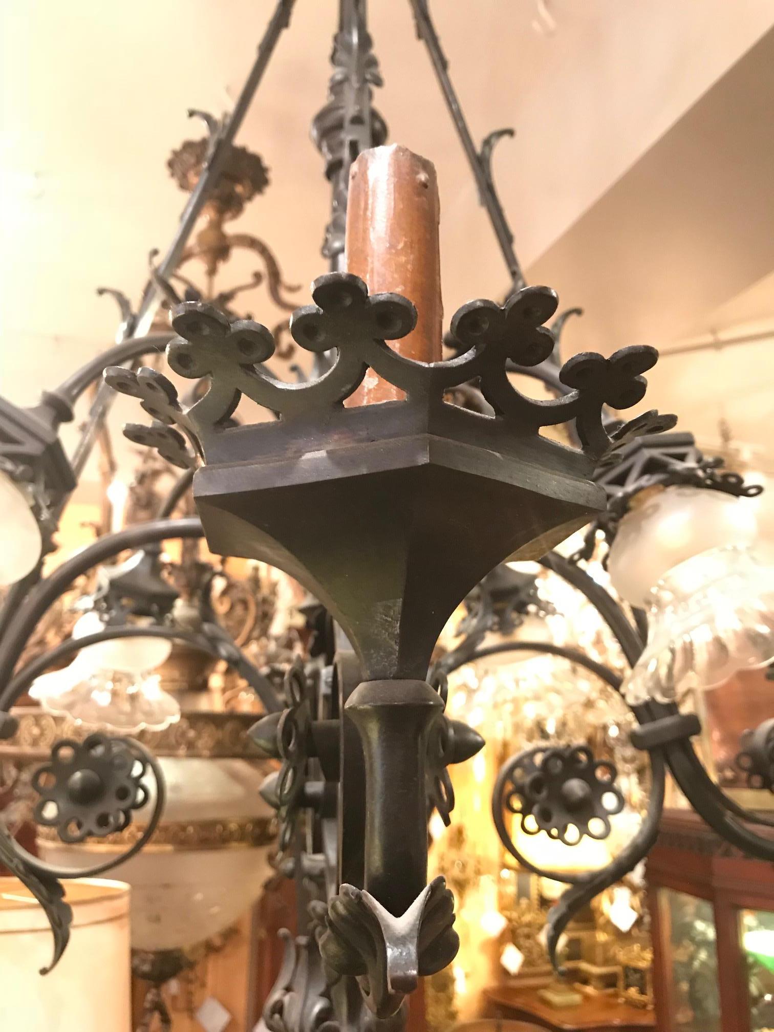 This late 19th century Gothic style patinated bronze  chandelier  was once a gasolier,. It has eight arms, four  flowing down from the foliate decorated crown . The other four upturned;  all with scrolling and leaf decorated arms, . The clear shades