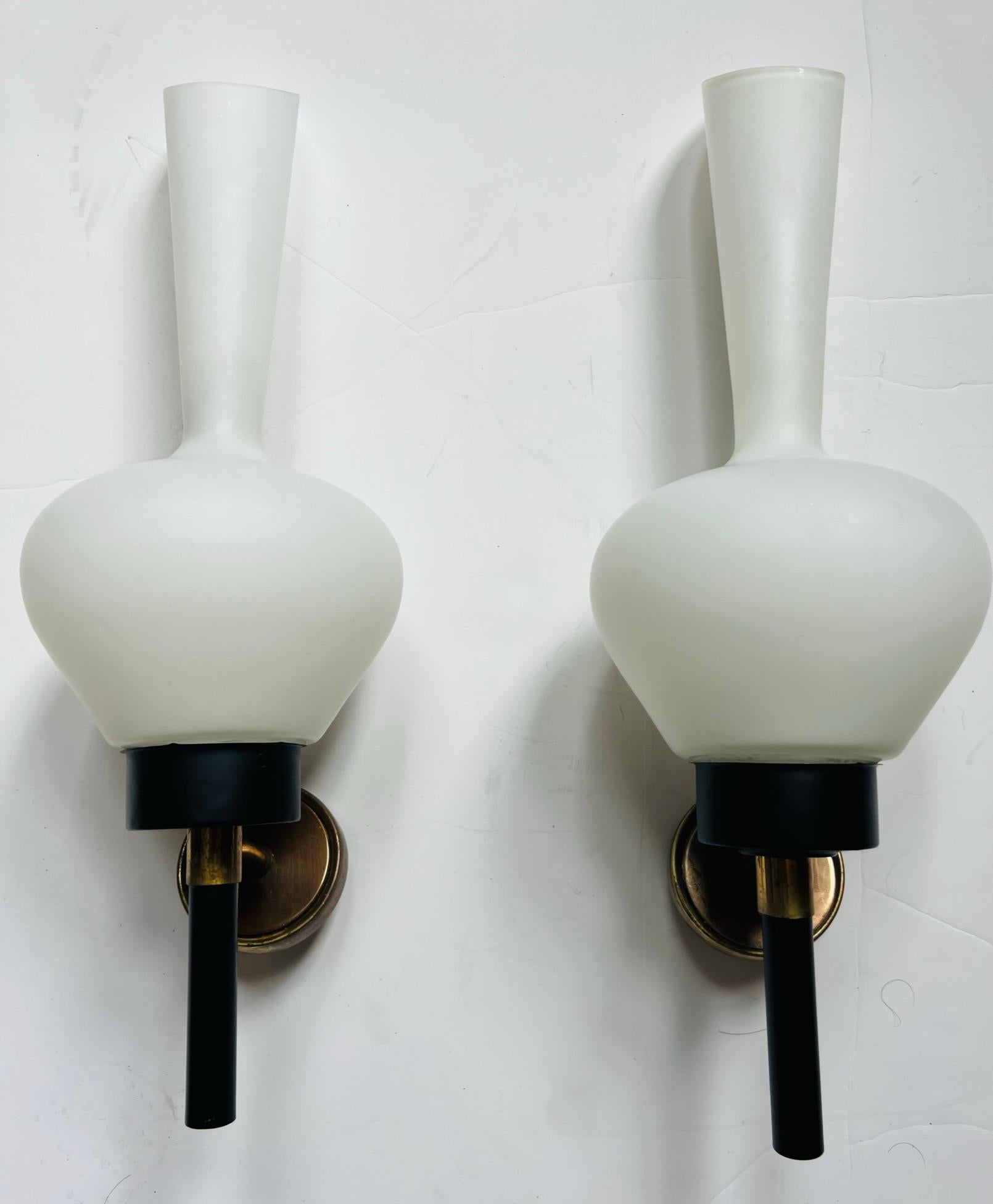 A beautiful large pair of 1950s French wall lights with white elongated glass shades and black enamel and aged brass fixtures. Matching 5” back plates provided. Rewired.Rare.. 7” depth with added American backplate. Last two pictures show the added