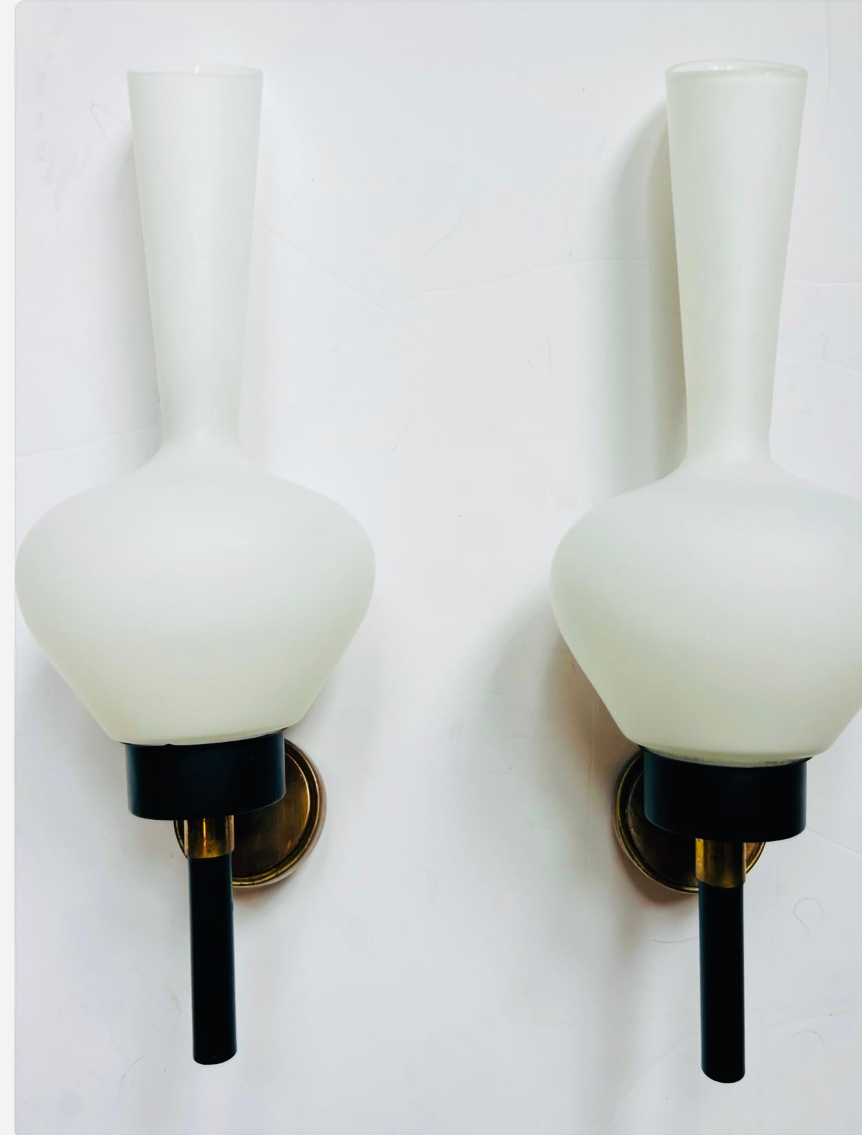 A beautiful large pair of 1950s French wall lights with white elongated glass shades and black enamel and aged brass fixtures. Matching 5” back plates provided. Rewired.Rare.. 7” depth with added American backplate. Last two pictures show the added