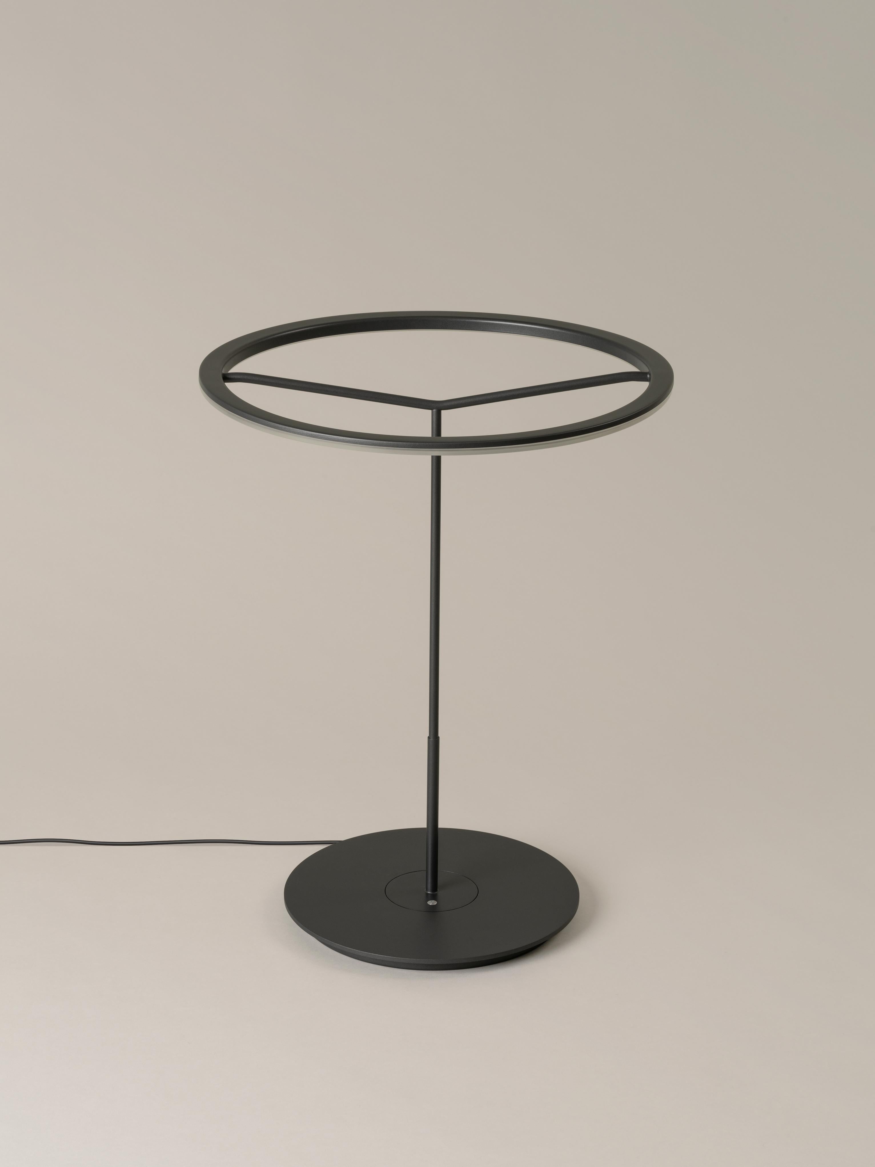 Large Graphite Sin table lamp by Antoni Arola
Dimensions: D 45 x H 58 cm
Materials: Metal.
Available in white or graphite, with or without shade.

A lamp that combines simplicity and technology to create a lucent ring of light suspended in the
