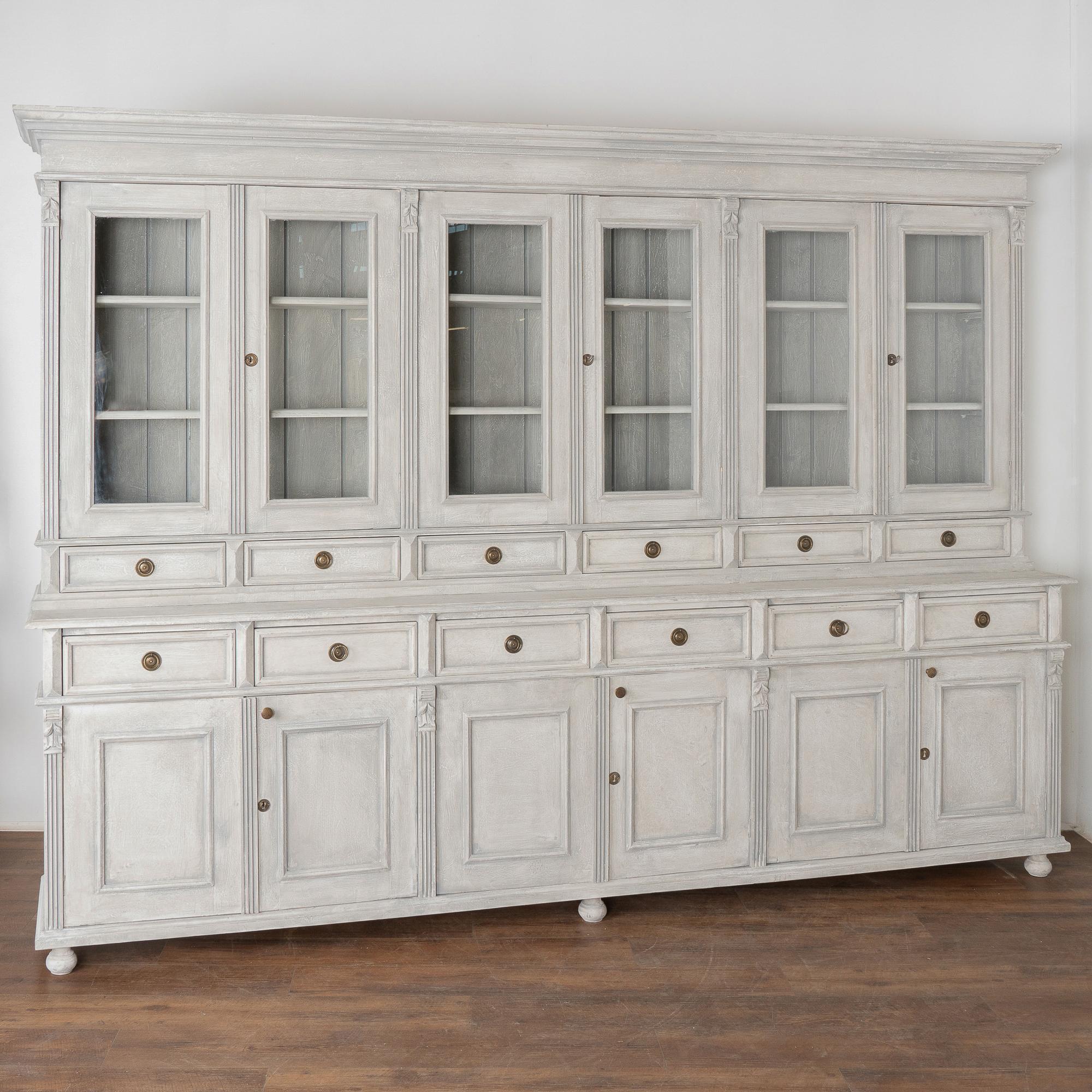 This striking large pine bookcase or display wall unit is a reproduction made in Europe and breaks down into two large upper and lower sections.
The lovely gray painted professional finish has white undertones, please examine close up photos to