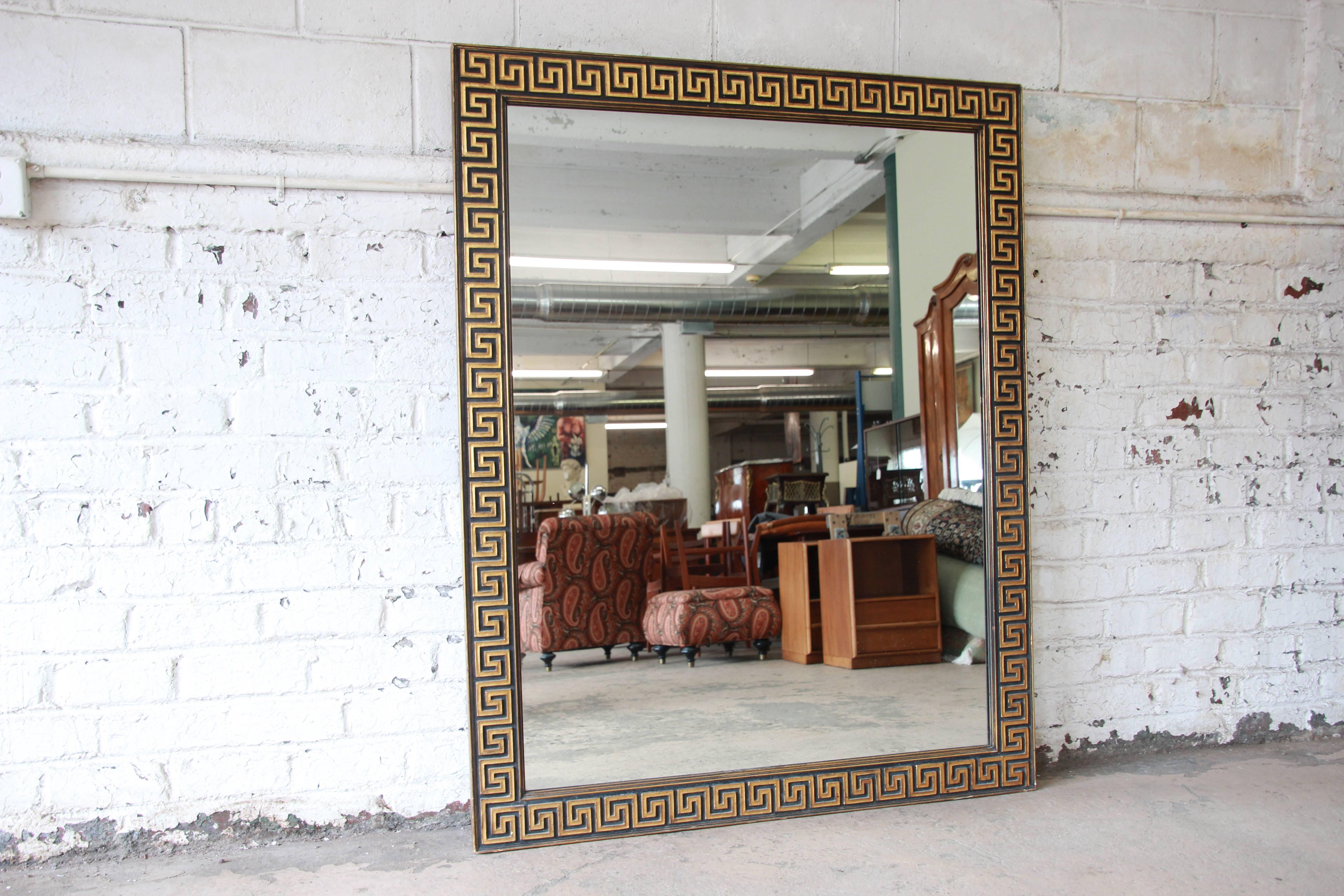 A gorgeous Hollywood Regency large mirror in a gold leaf and black wood frame with Greek key design. The frame retains its character with the original patina. It is in good condition, with minor wear from age and use.