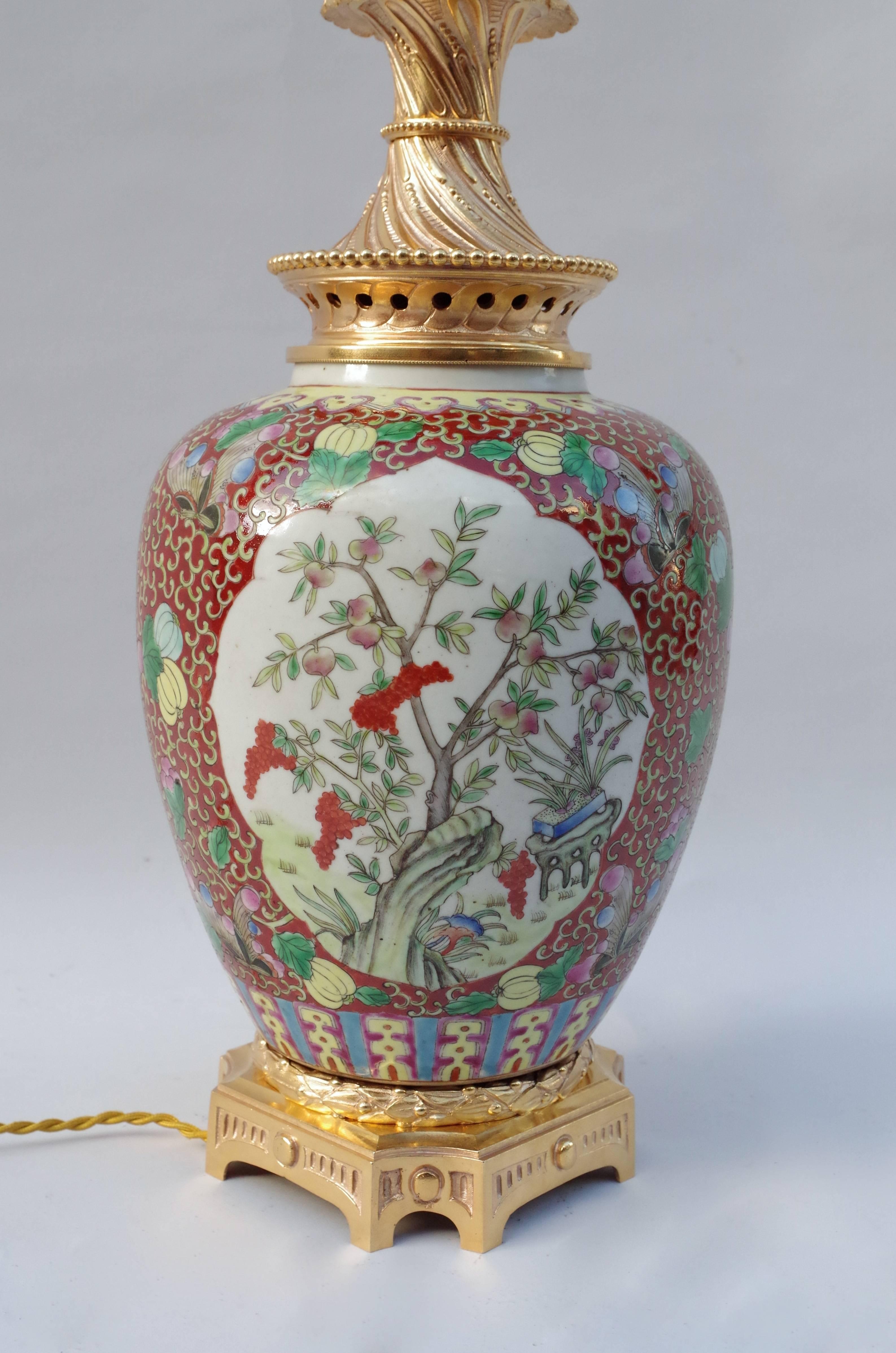 Large vase shaped porcelain lamp.
Green family porcelain on a red background, decorated with interlaces, flowers and butterflies. Plants in reserve in two white background cartouches as Chinese gooseberries, prunus blossoms, carnation and
