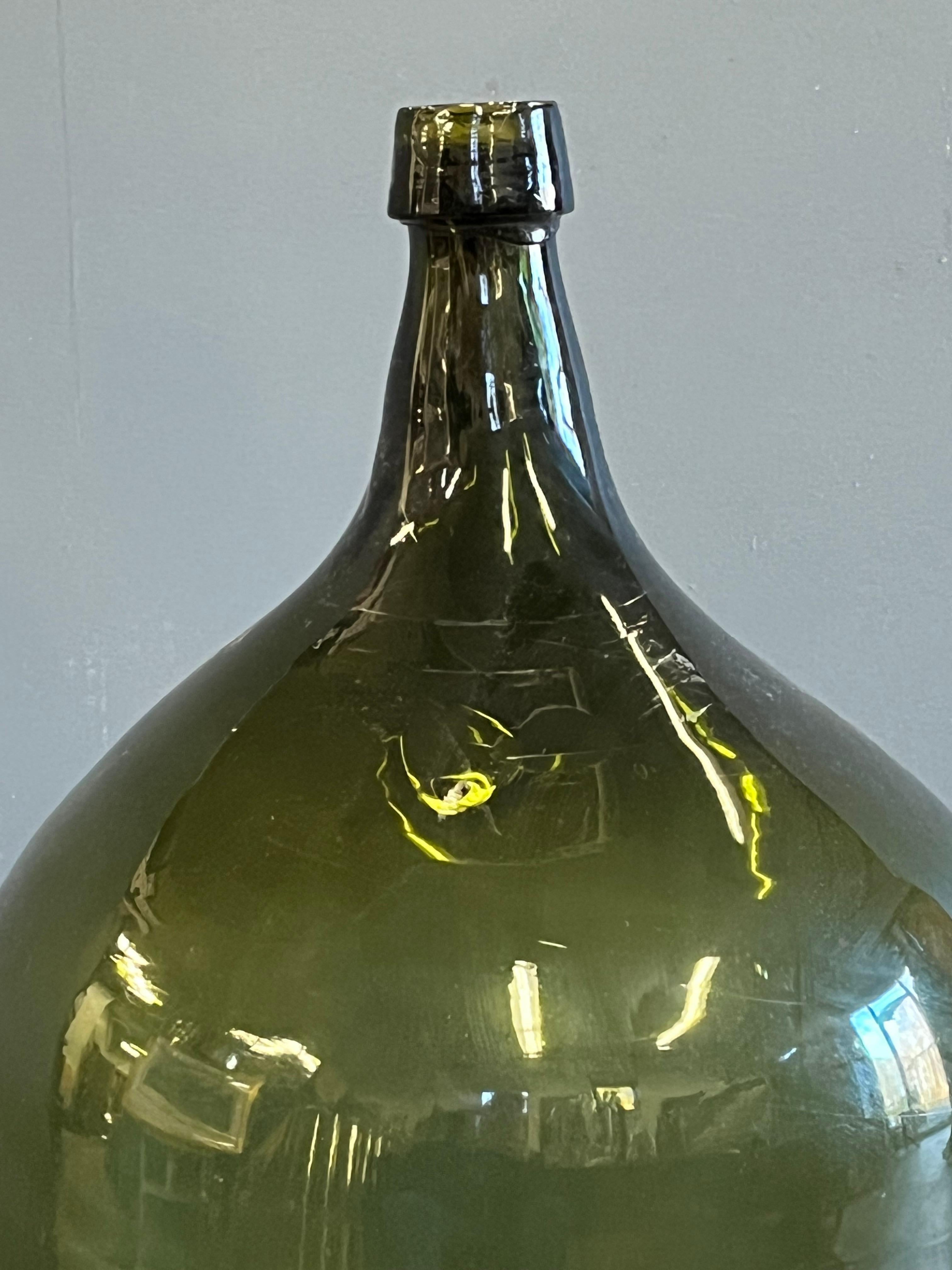 A large blown glass demijohn in deep olive green, with applied tooled lip and large iron pontil scar on base. Circa 1870 