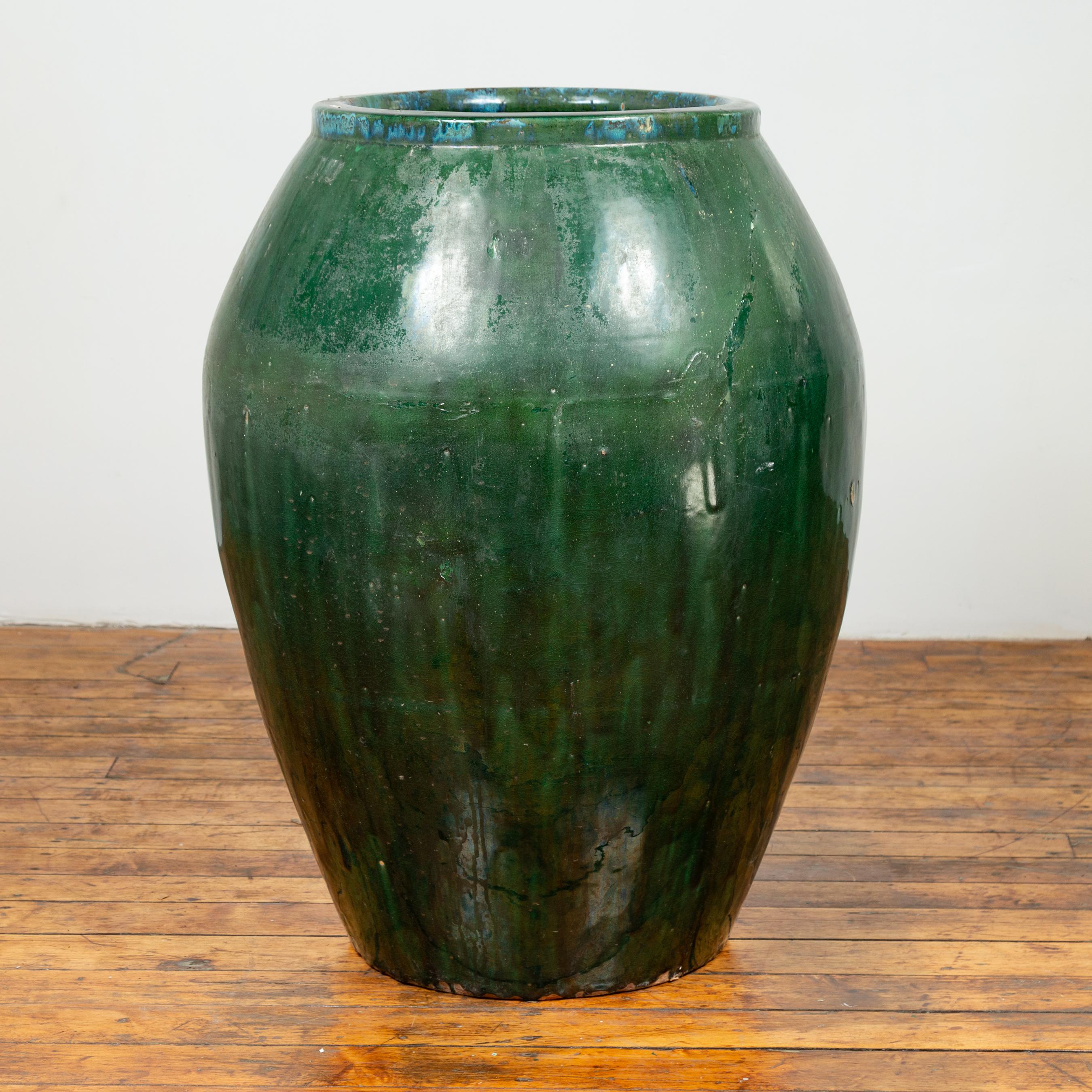 A large Asian green glazed ceramic jar from the early 20th century with nicely weathered appearance. Charming us with its large proportions and slightly weathered appearance revealing its age and use, this green glazed ceramic jar features a narrow