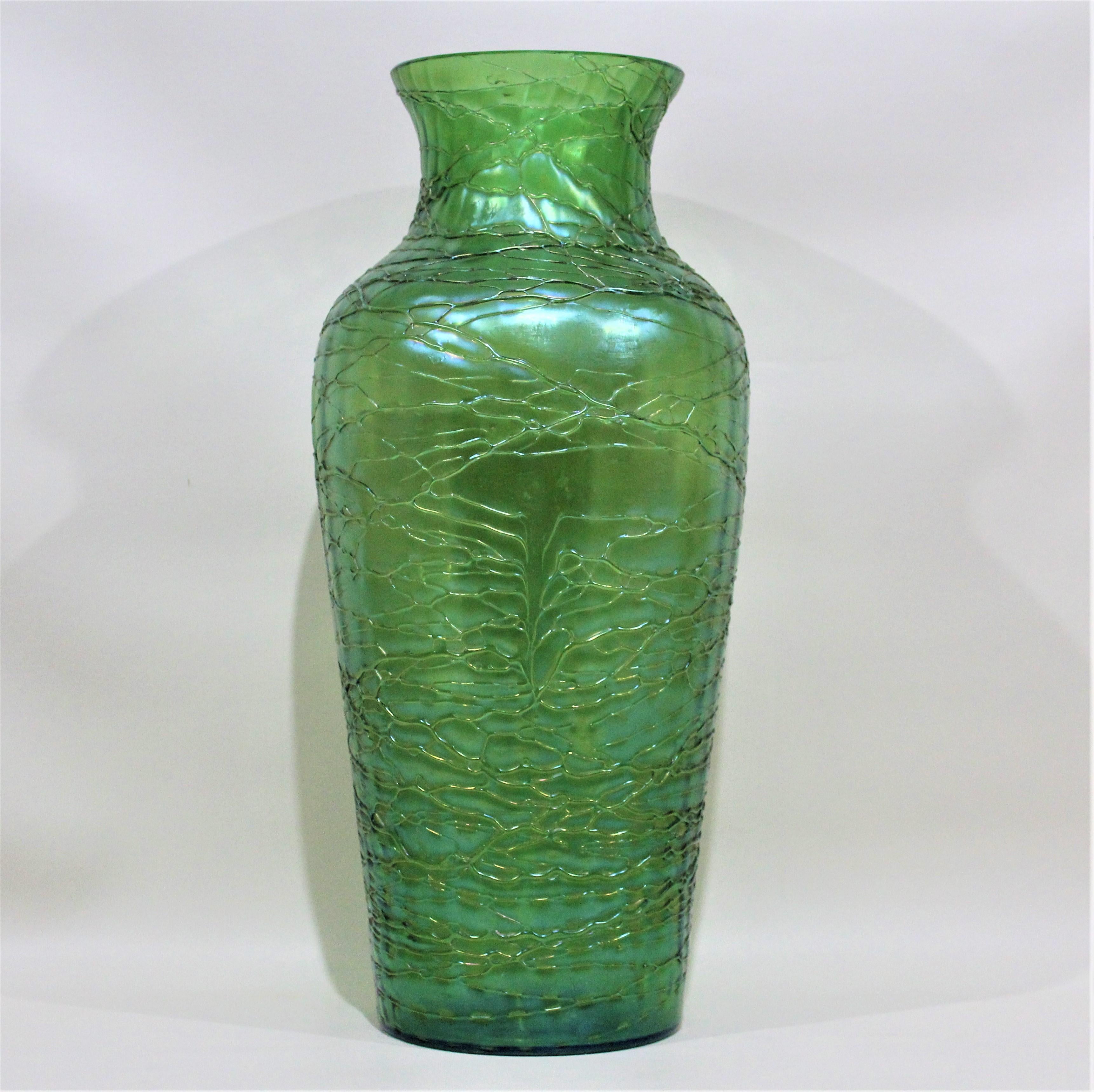 This substantial iridescent deep green vase was made by Loetz in and around the Early 20th century in an Arts & Crafts or Art Nouveau style. The entire vase is artfully decorated with hand applied threading in the same color, and accentuates the
