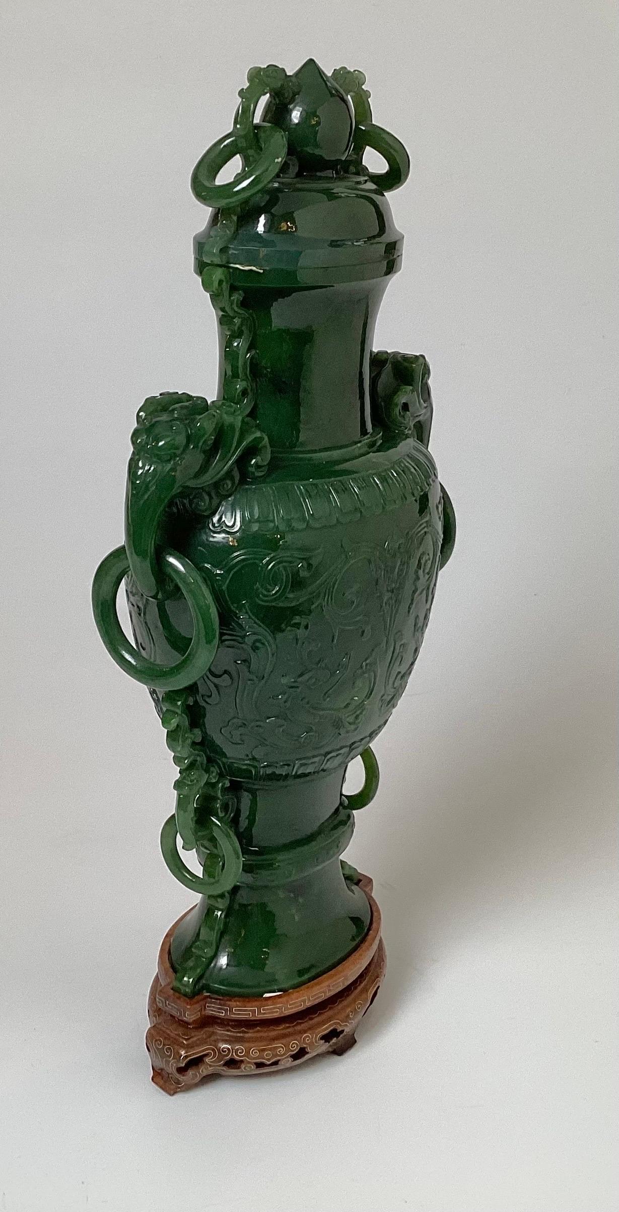Vase en jade vert sculpté avec couvercle. Le jade vert foncé avec des poignées en forme d'éléphant et d'anneau et une base en bois personnalisée. 12,75 pouces de hauteur, y compris la base. Début du 20e siècle, période Qing/République, Chine.