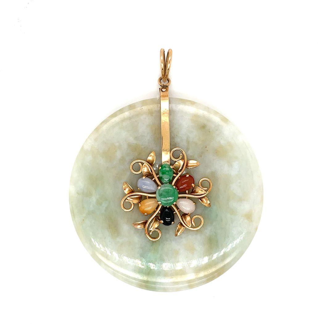 This stunning pendant features a 54 mm jadeite jade disc set in 14K gold wirework, with a floral design at center featuring pear shaped cabochon of various shades of jadeite, including brown, black, green, lavender, orange and pink. 

This precious