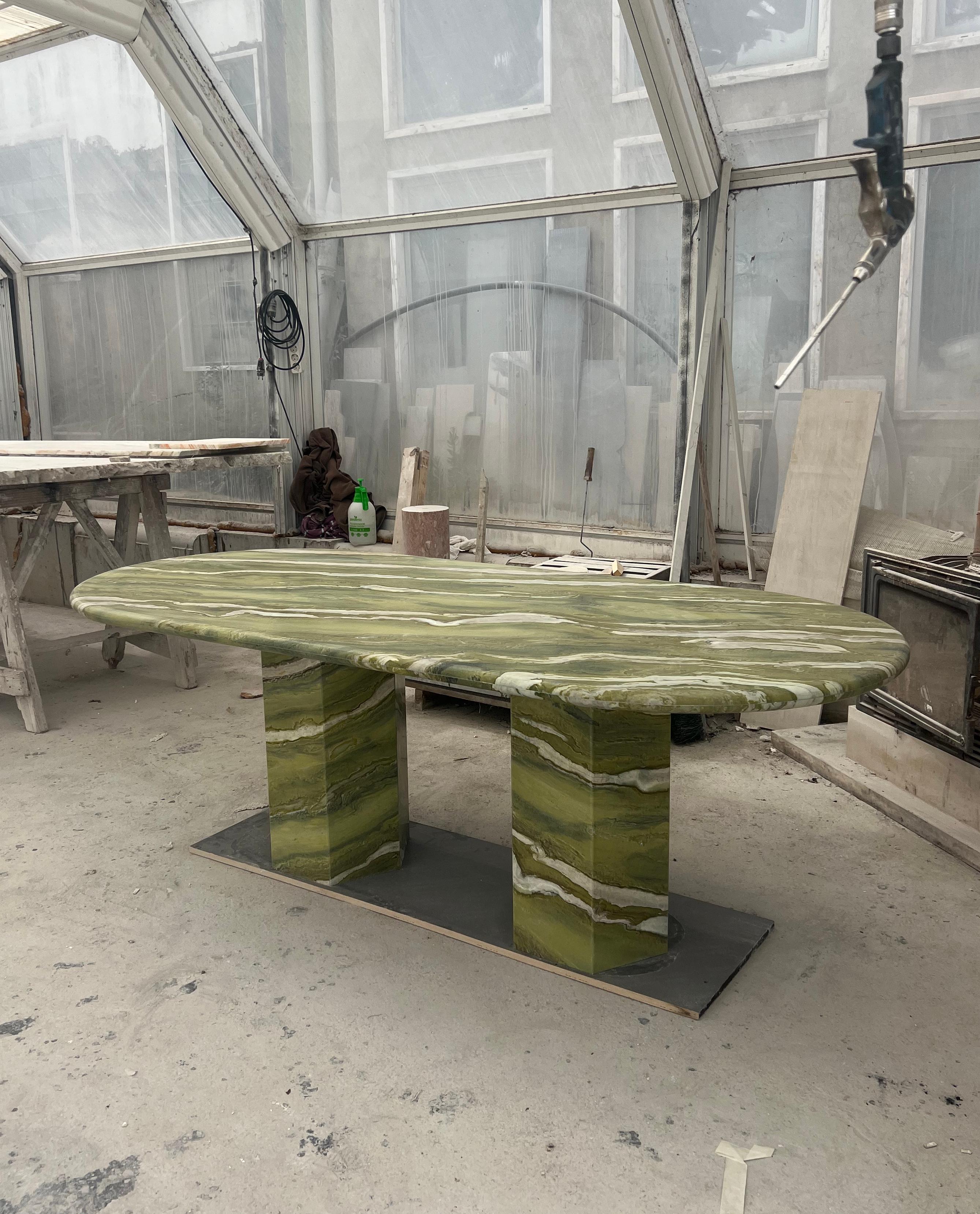 Cette table minimaliste est fabriquée à partir d'un seul matériau, avec un plateau épais de 4 cm à bord incurvé en marbre vert avec des veines uniques, qui repose élégamment sur deux pieds hexagonaux, pratiquement positionnés pour accueillir