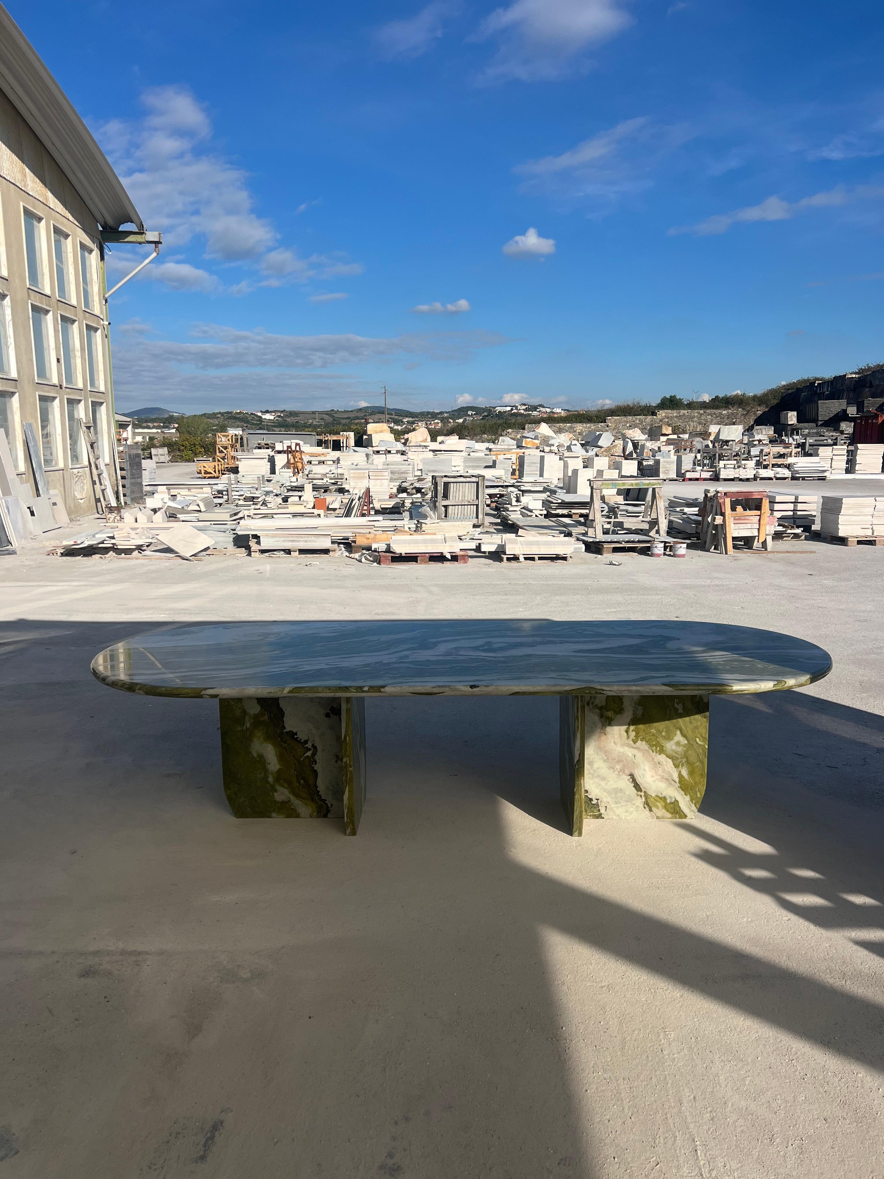 Cette table minimaliste est fabriquée à partir d'un seul matériau, avec un plateau épais de 4 cm à bord incurvé en marbre vert avec des veines uniques, qui repose élégamment sur deux pieds hexagonaux, pratiquement positionnés pour accueillir