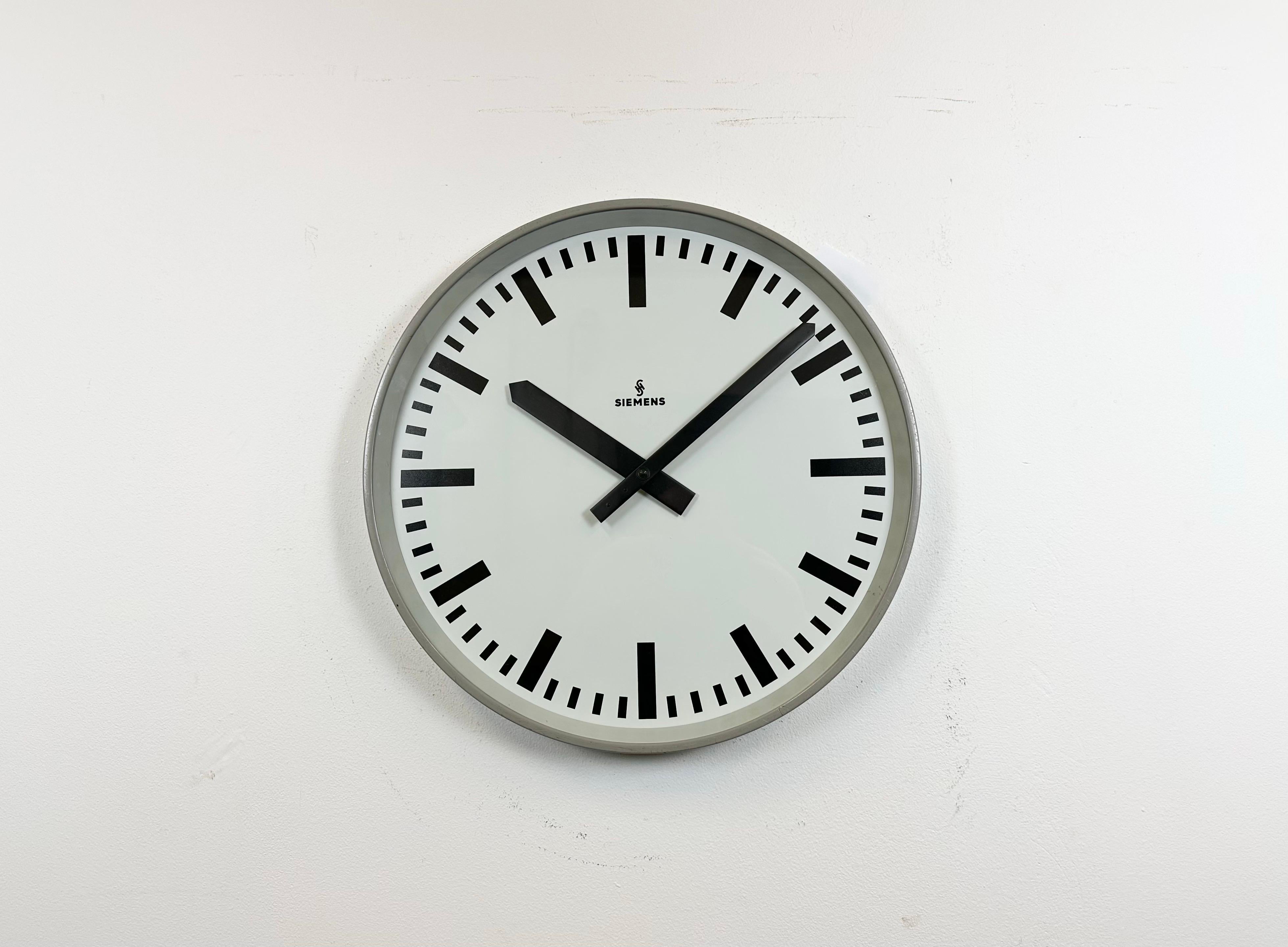 This wall clock was produced by Siemens in Germany during the 1970s. It features a grey iron frame, a metal dial and a clear glass cover. The piece has been converted into a battery-powered clockwork and requires only one AA-battery. The weight of