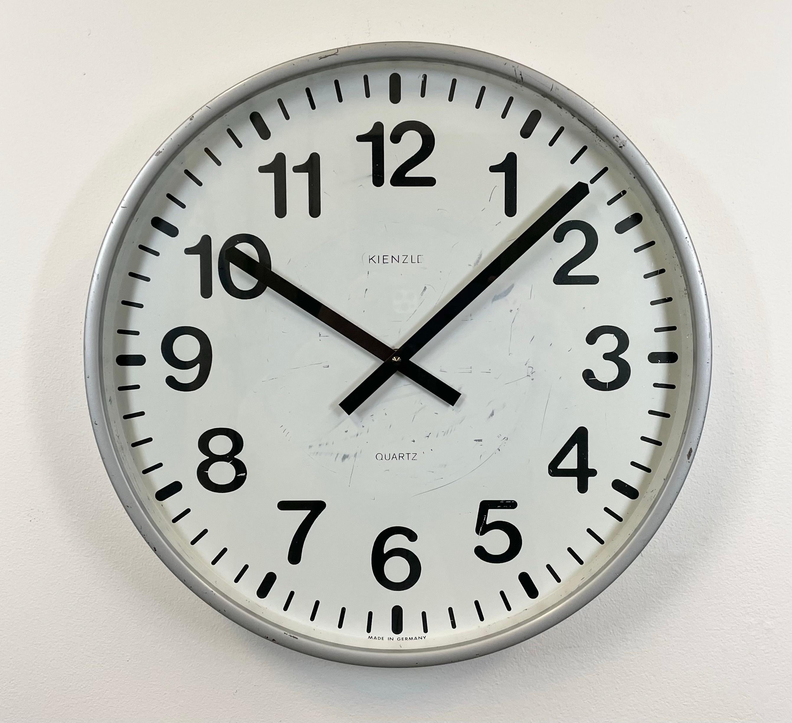 Vintage Industrial wall clock made by Kienzle in Germany during the 1980s. It features a grey iron frame, a white metal dial, an aluminium hands and a clear glass cover. The piece has been converted into a battery-powered clockwork and requires only