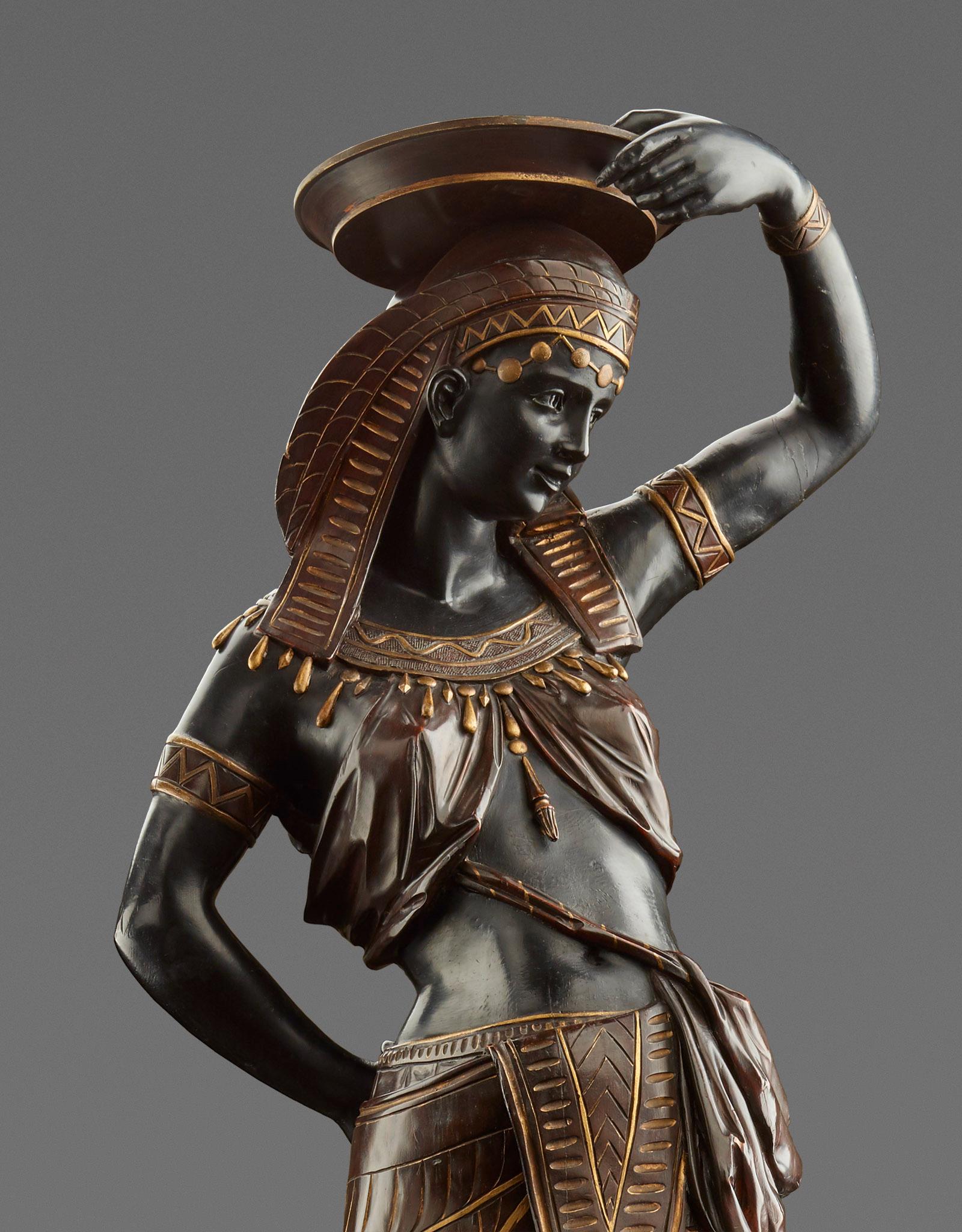 Venice, c. 1865
Wood, carved and set, partially gilded. On a pedestal decorated with lancet leaves and a surrounding animal frieze with four kneeling servants, the impressive figure of a graceful, richly decorated Egyptian dancer, carrying a bowl