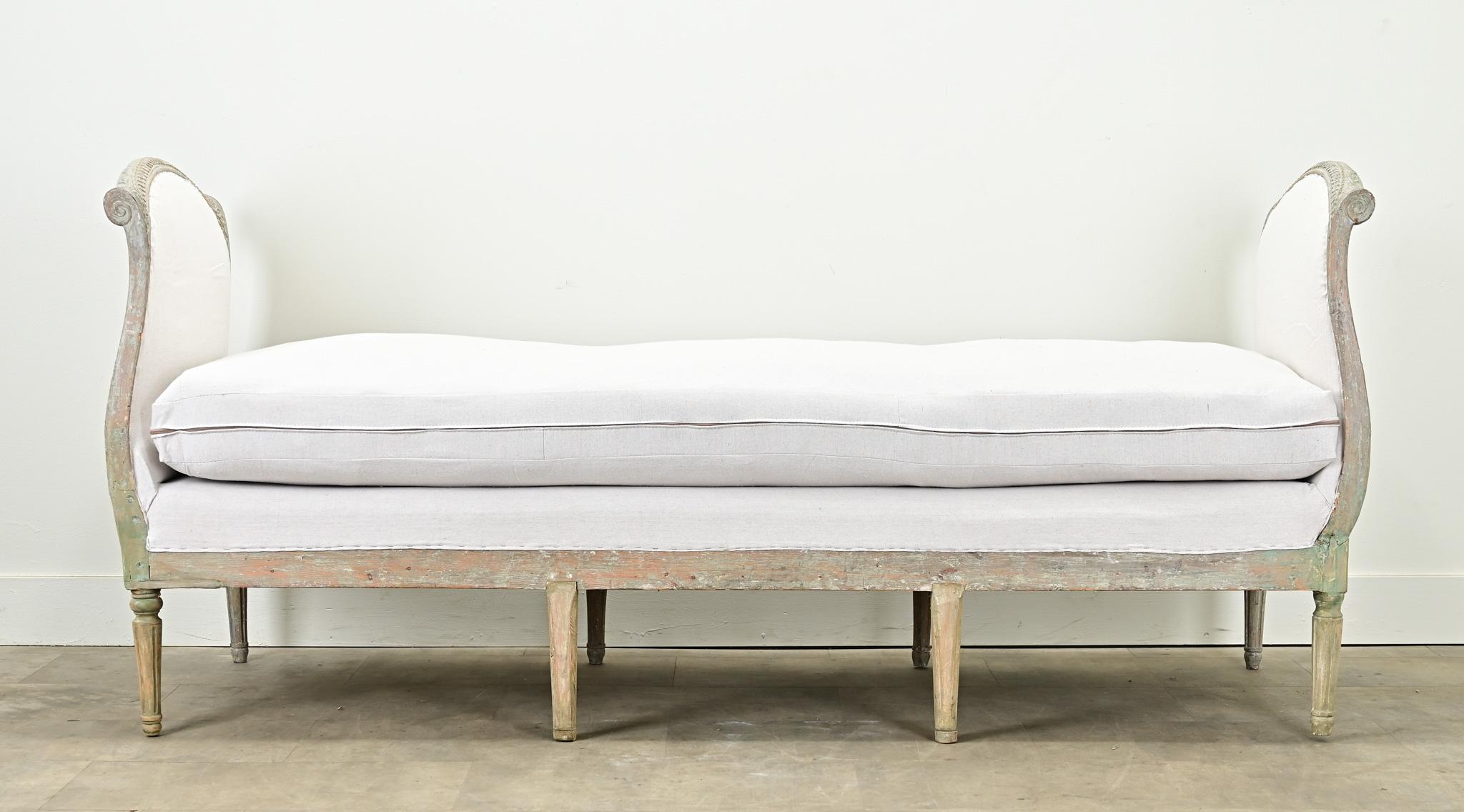 An impressive and elongated Swedish Gustavian daybed from the 1790’s. The bed frame is all hand carved with bell flower motifs and guilloche patterned carvings under layers of light blue-gray paint. Recently tightened and upholstered with new