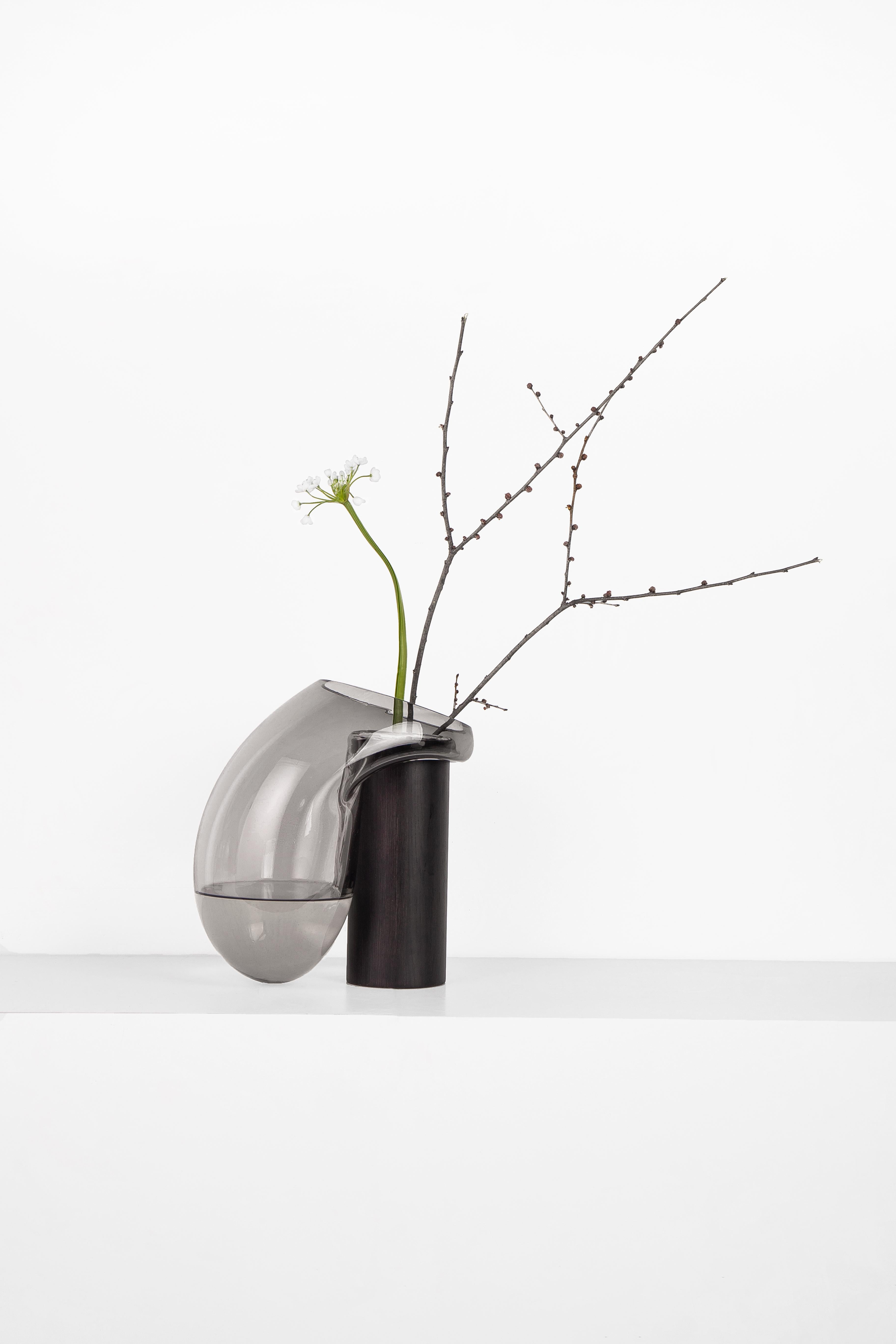Vaso grande Gutta Boom CS3 di NOOM
Dimensioni: L. 20 x P. 21 x H. 30 cm 
Materiali: Vetro soffiato grigio neutro e rovere rivestito internamente con resina epossidica.

I vasi scultorei in vetro 