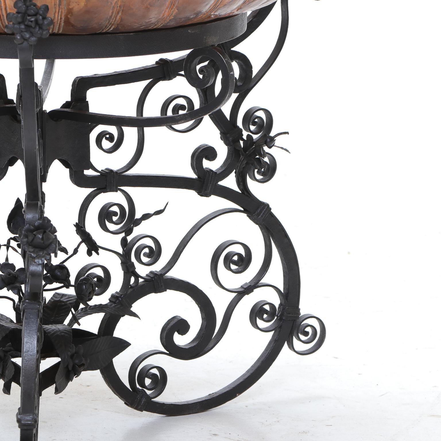 Großer, handwerklich gefertigter Pflanzkübel aus gehämmertem Kupfer, der in einen schmiedeeisernen, geschwungenen Sockel eingesetzt ist.