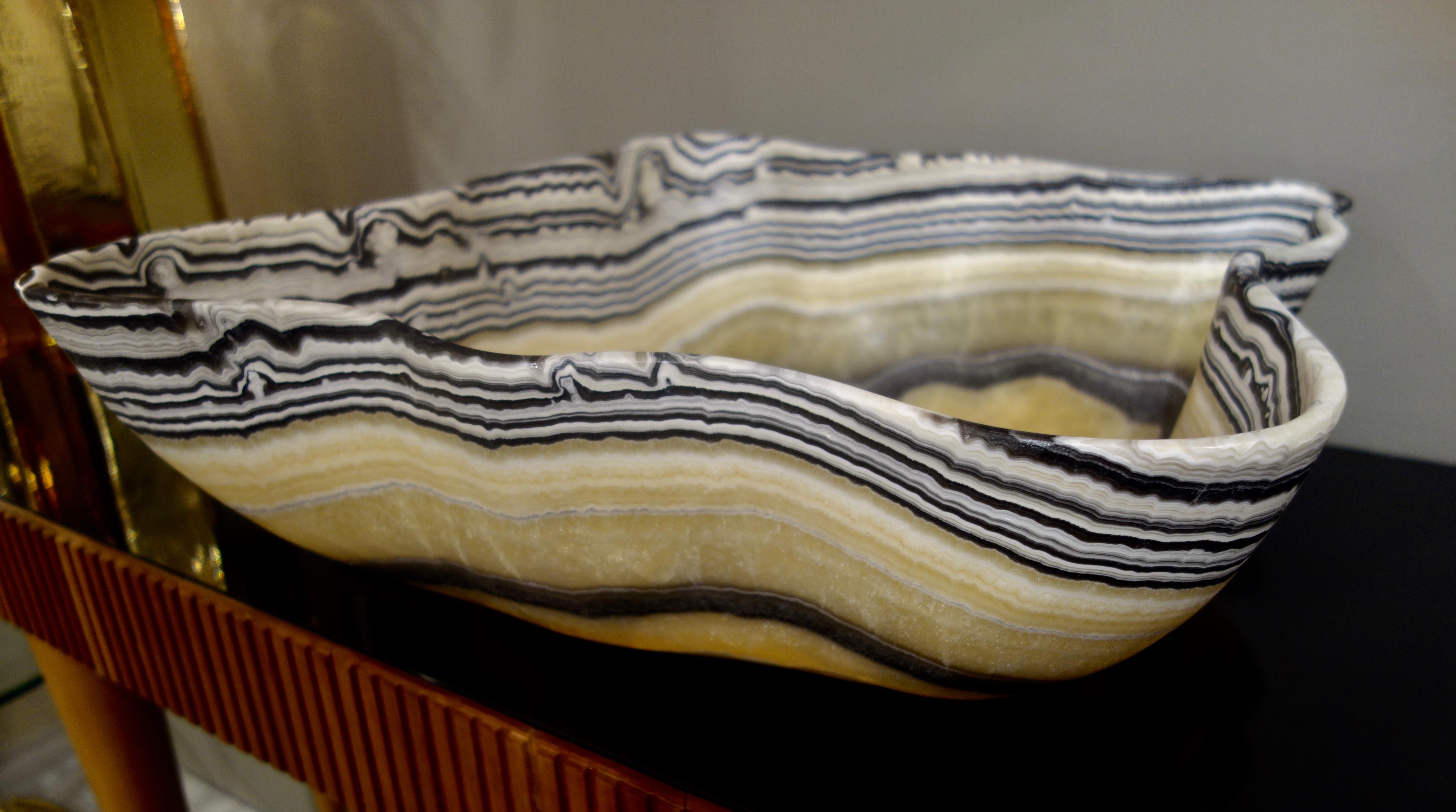 A large hand carved onyx bowl or centerpiece with zebra striped rim in shades of gold, charcoal gray and white with natural negative spaces.