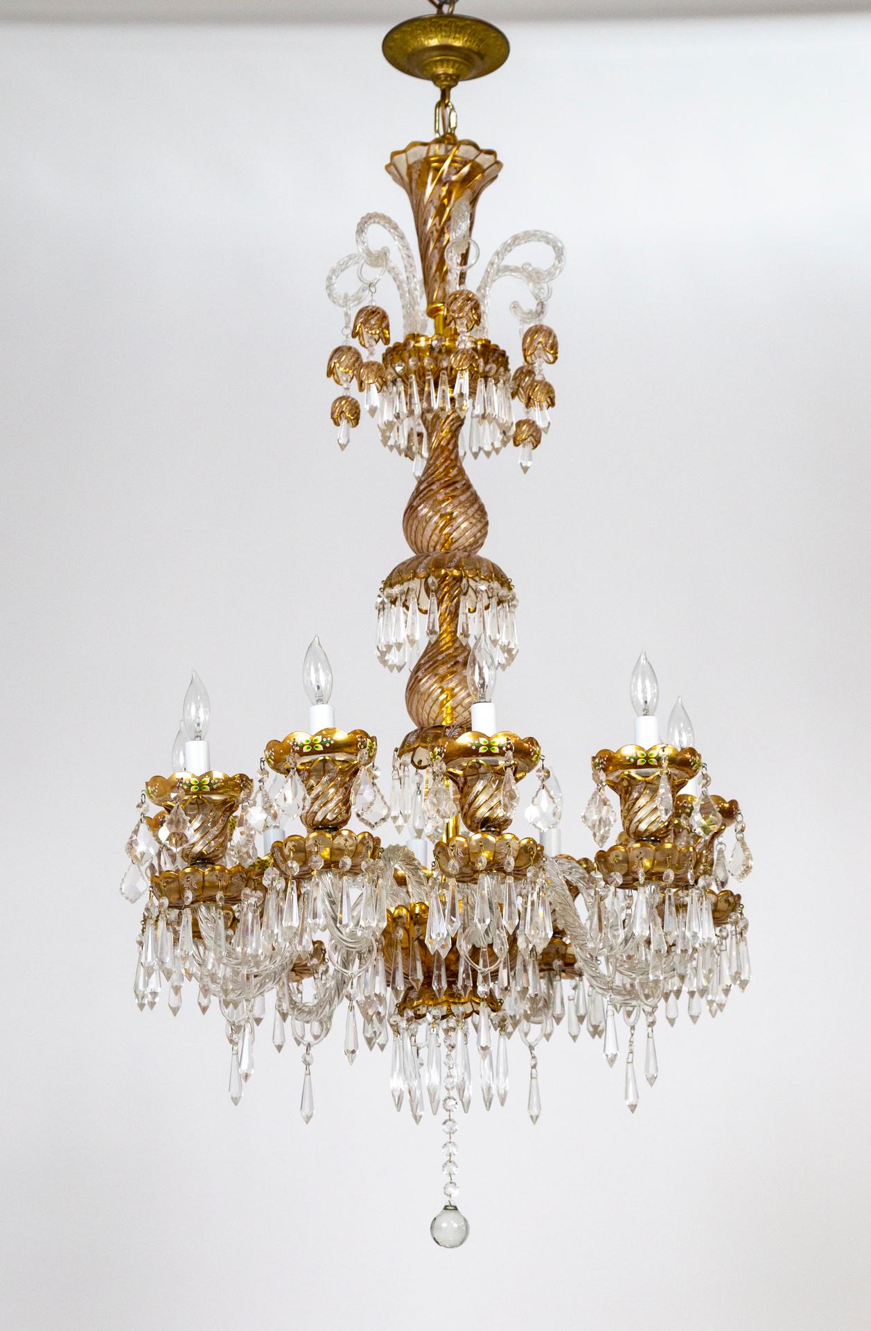Enchanting, 10 arm Bohemian glass chandelier.
Hand blown clear glass twisted arms and body. Hand enameled ornate detailing with floral motifs, 24kt gold embellishments. Faceted crystal spears, pendalogues and double bells. The elongated body is