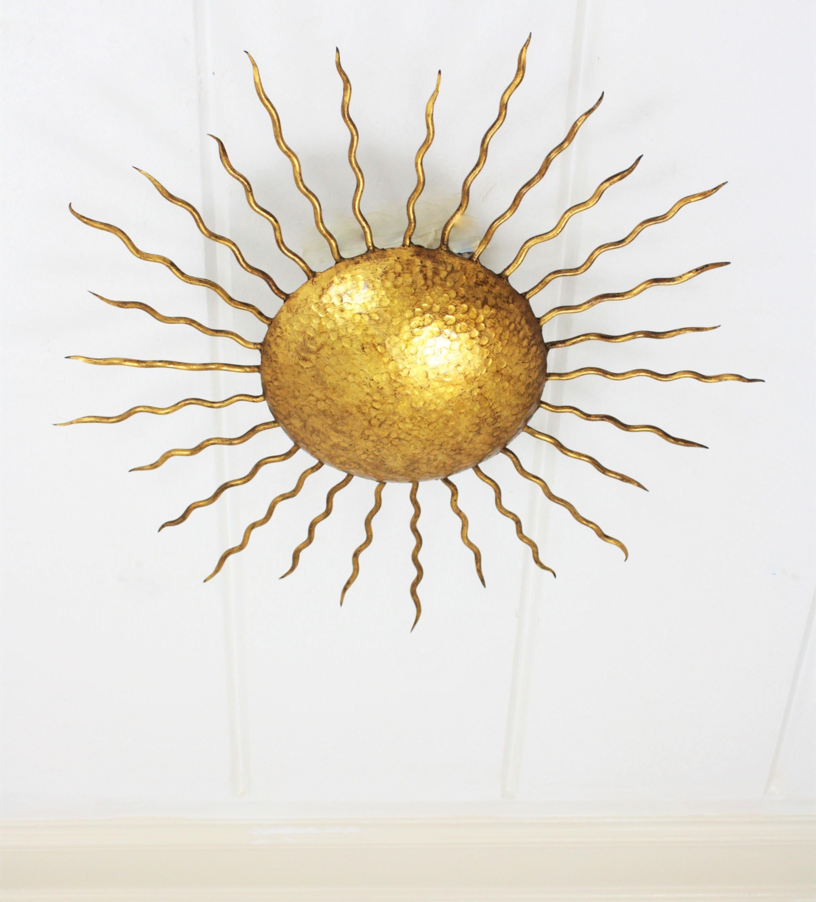 Gold leaf gilt iron sunburst light fixture from the Brutalist period. Richly decorated in the center part with hand-hammered marks. Curly iron rays surrounding the central sphere Beautiful to place as ceiling light fixture but also as a wall sconce,