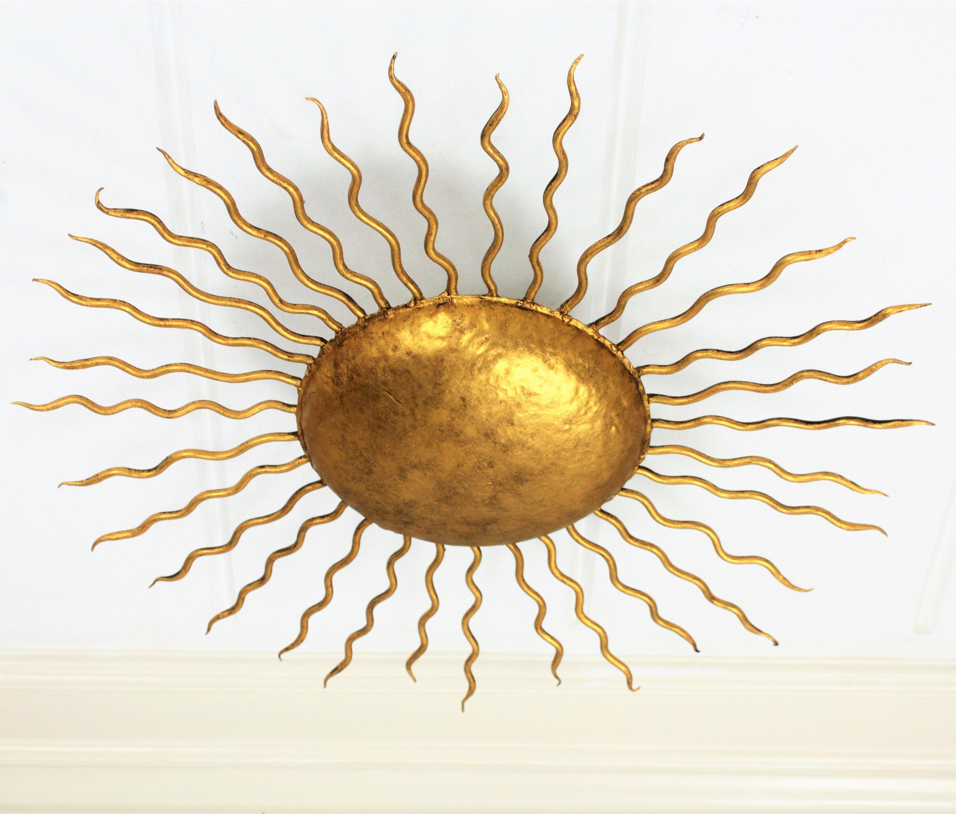 Beautiful hand-hammered gilt iron sunburst light fixture with Brutalist accents. Richly decorated with hand-hammered marks. It has curly iron rays in two sizes surrounding the central sphere. It can be placed as ceiling light fixture but also as a